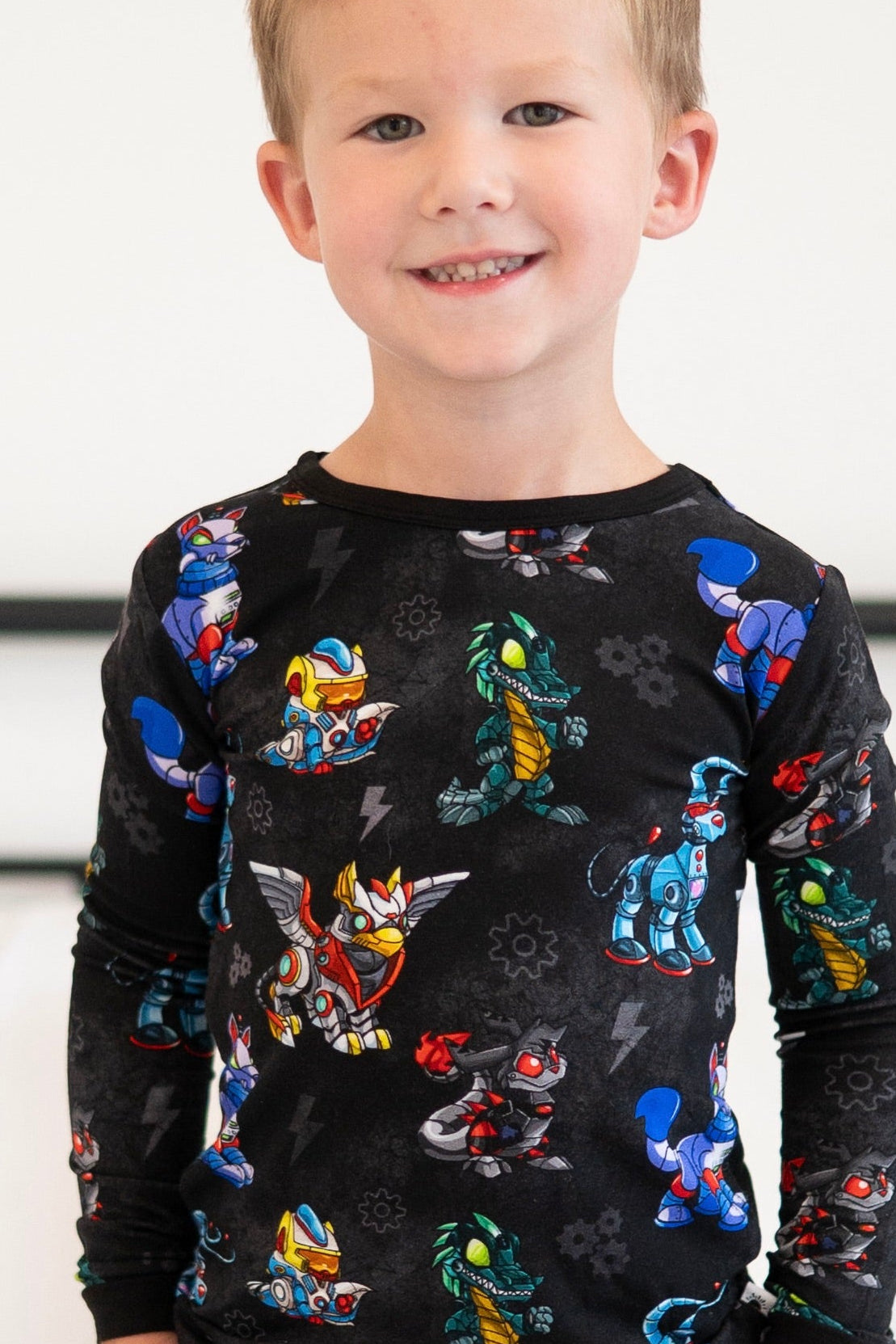 A young boy smiles wearing black pajamas with a robot and creature print.