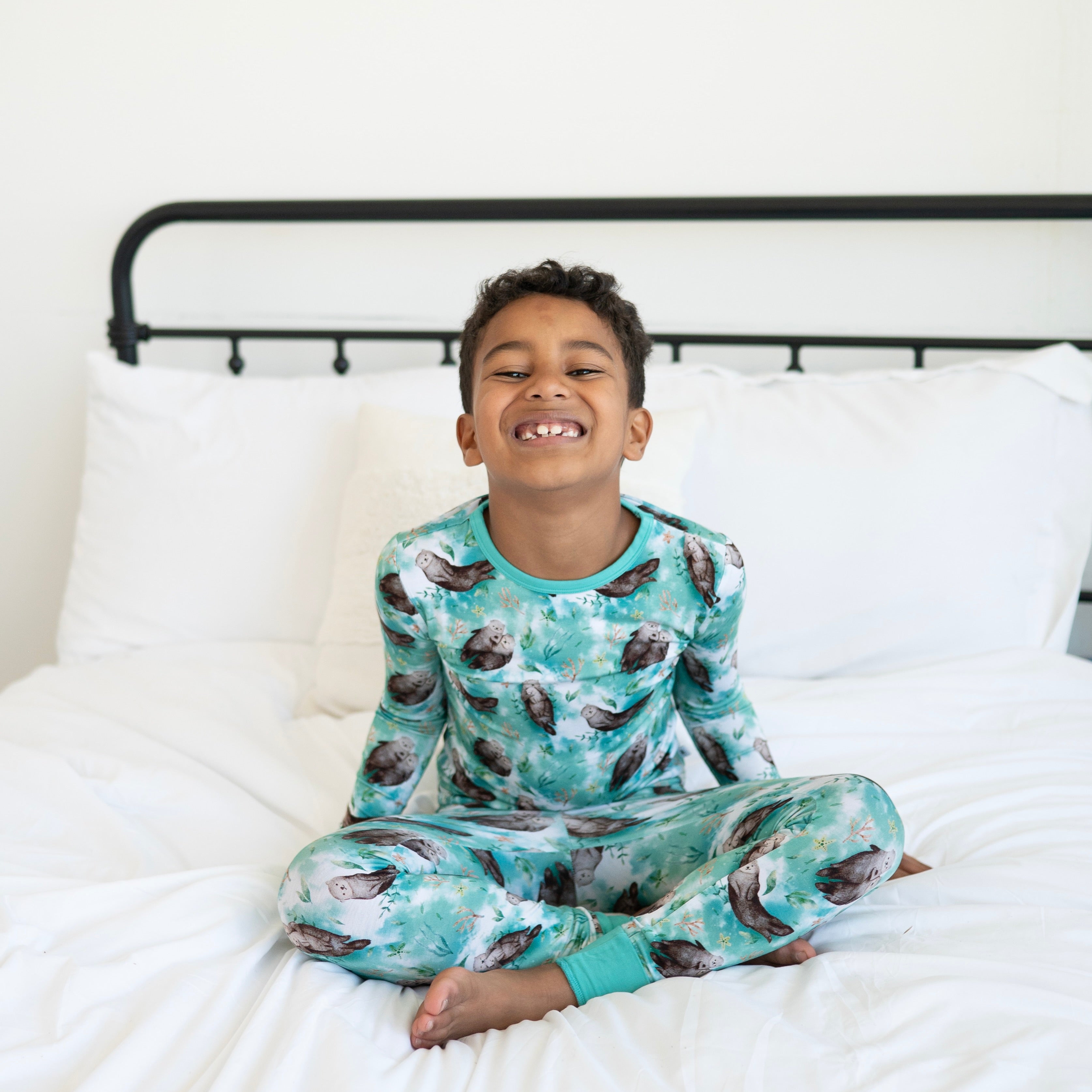 A young boy smiles while wearing a teal pajama set with an otter print.