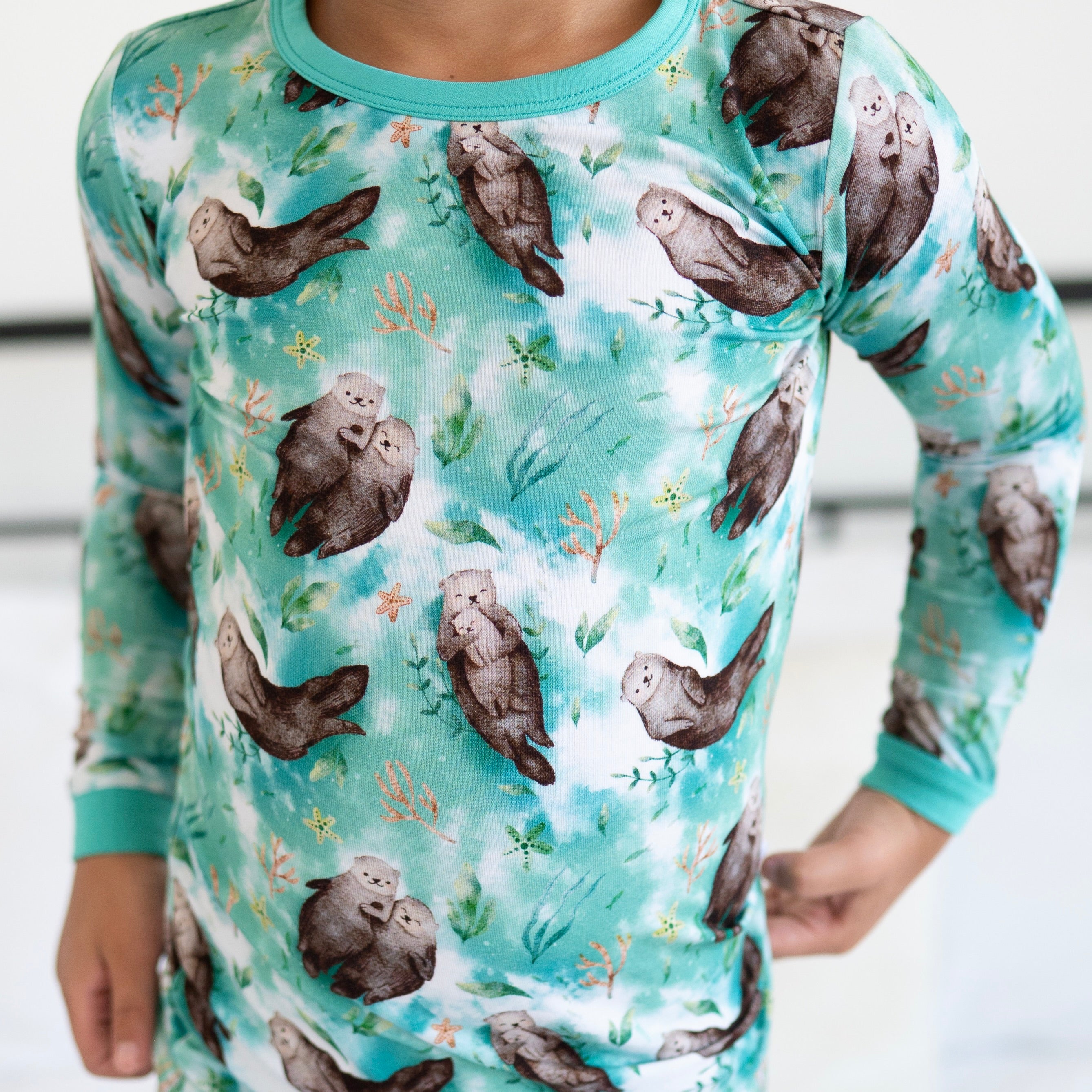 A child wears a long-sleeved pajama top with a watercolor print of otters and sea plants.