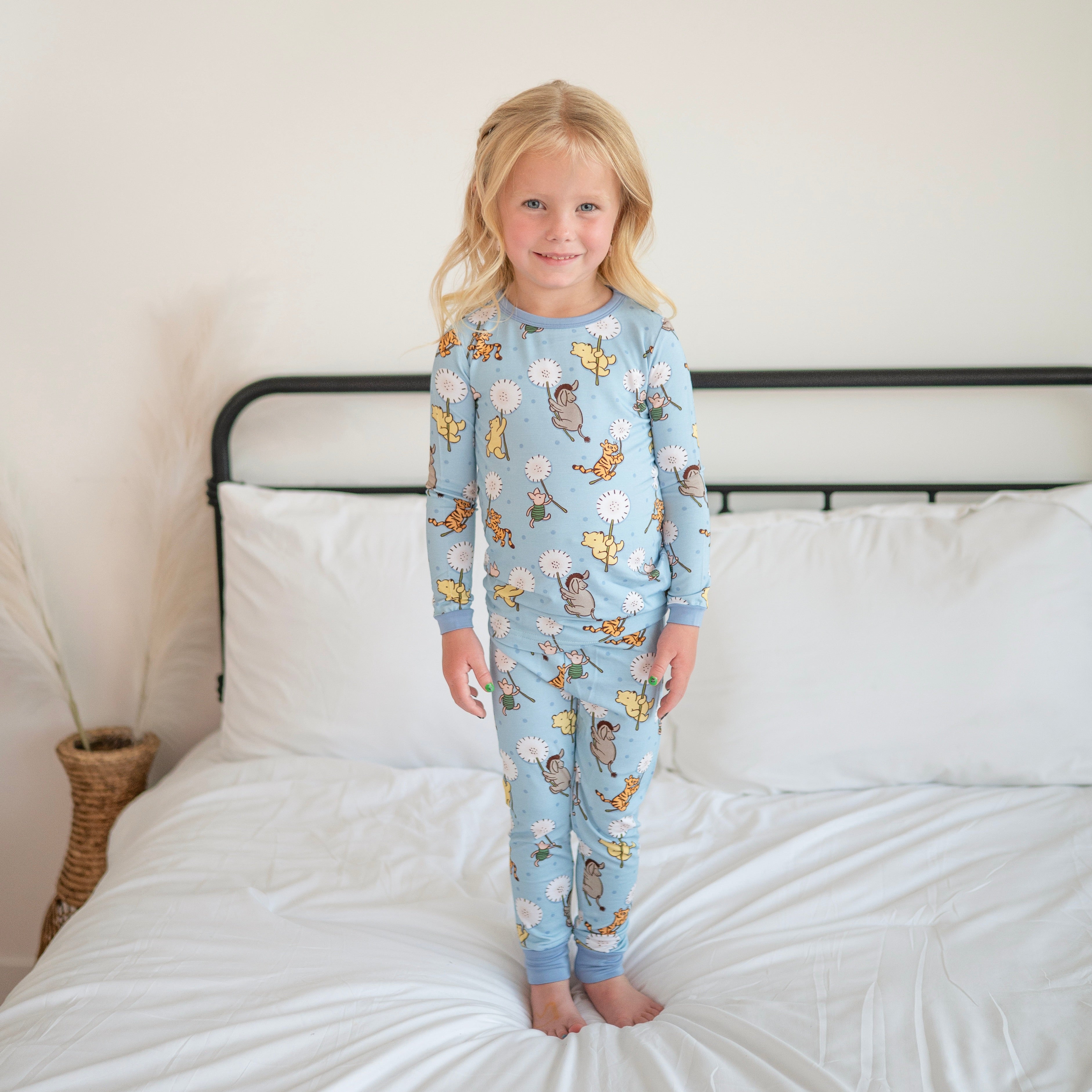 A young girl stands on a bed wearing blue pajamas