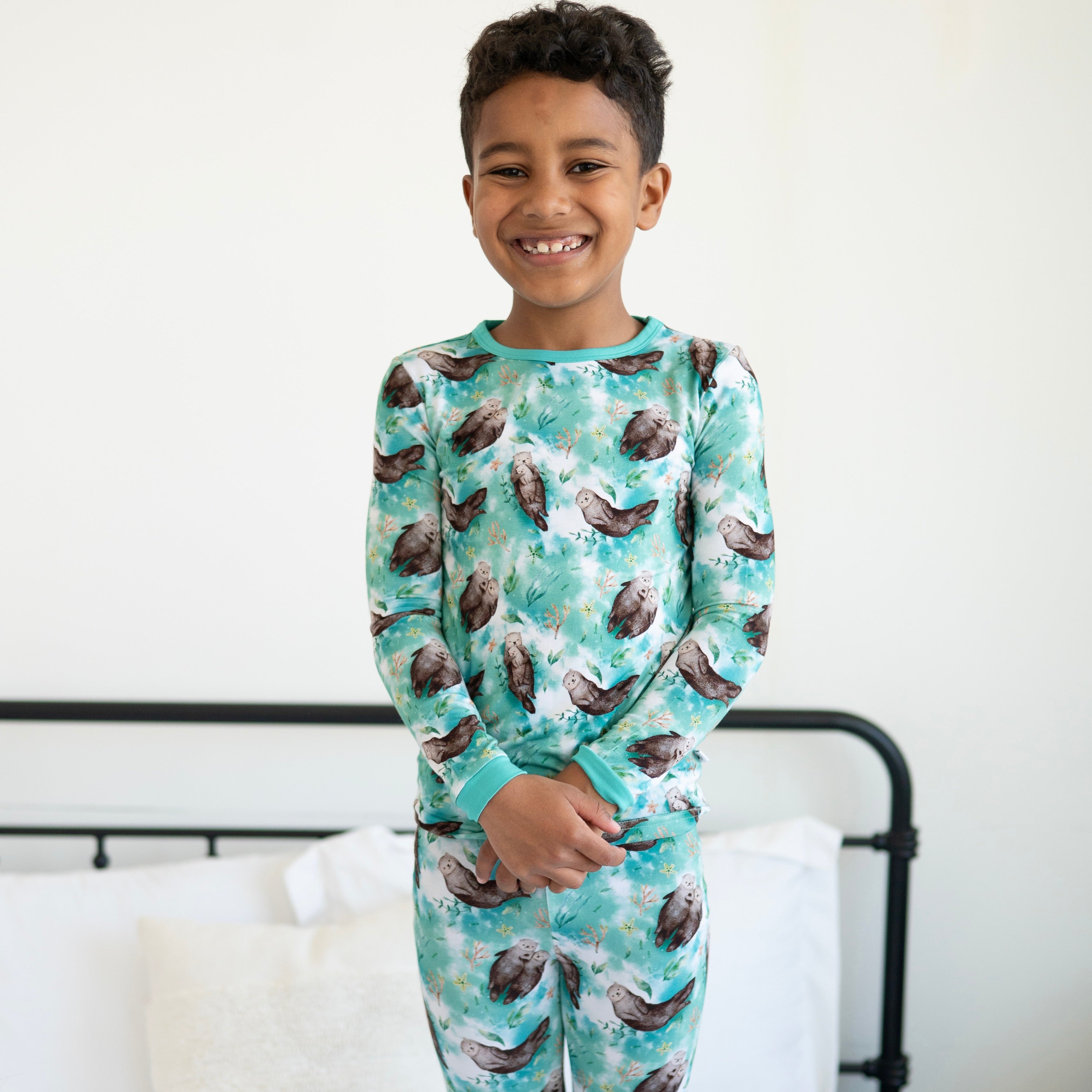 A young boy smiles wearing a long-sleeved pajama set with an otter print.