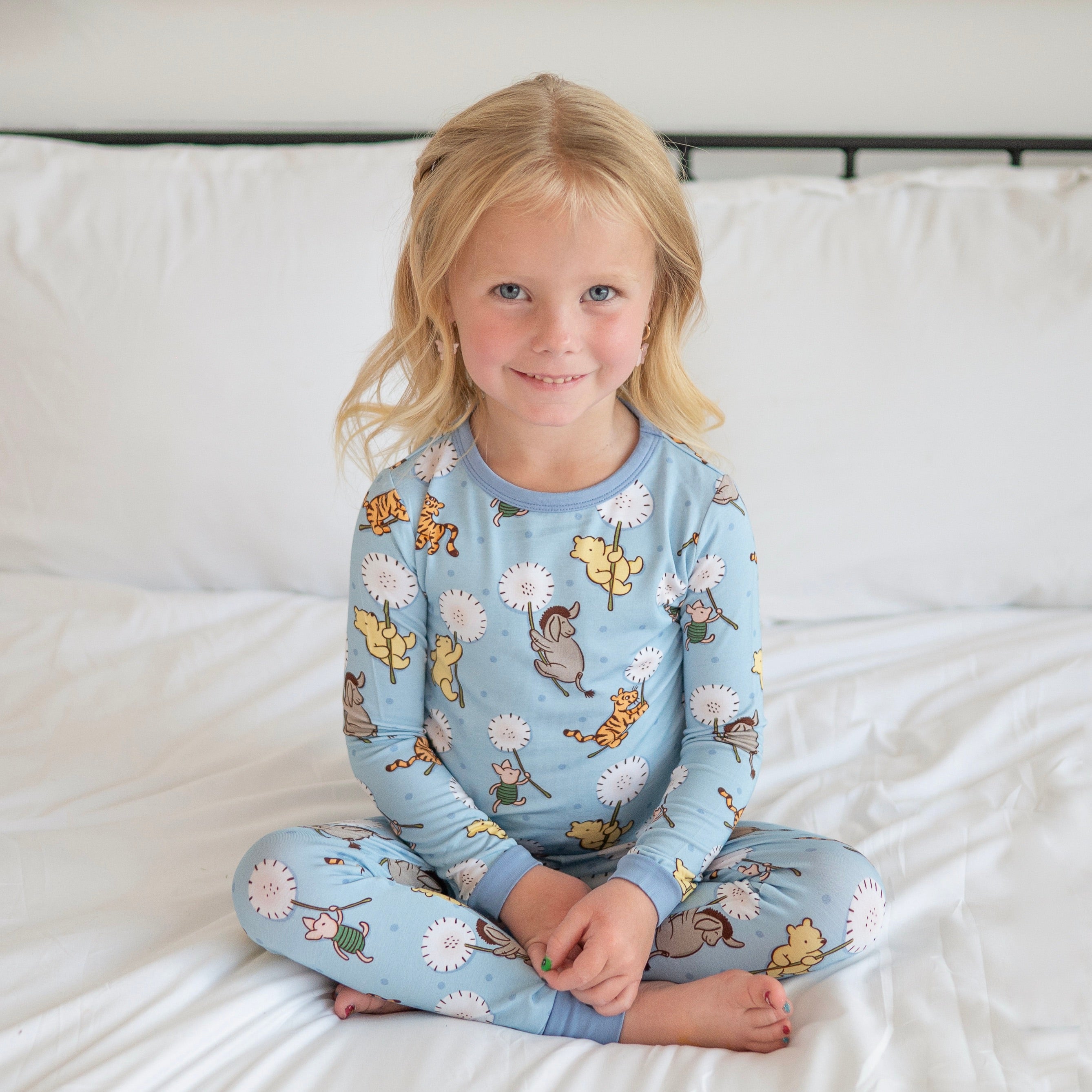 A young girl in blue pajamas sits cross-legged on a white bed.