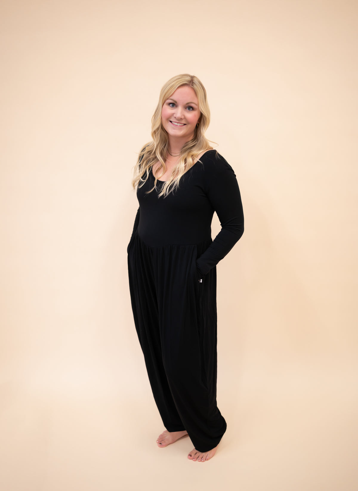 A woman smiles in a long-sleeve black Tencel Modal romper with a scoop neck and wide legs.