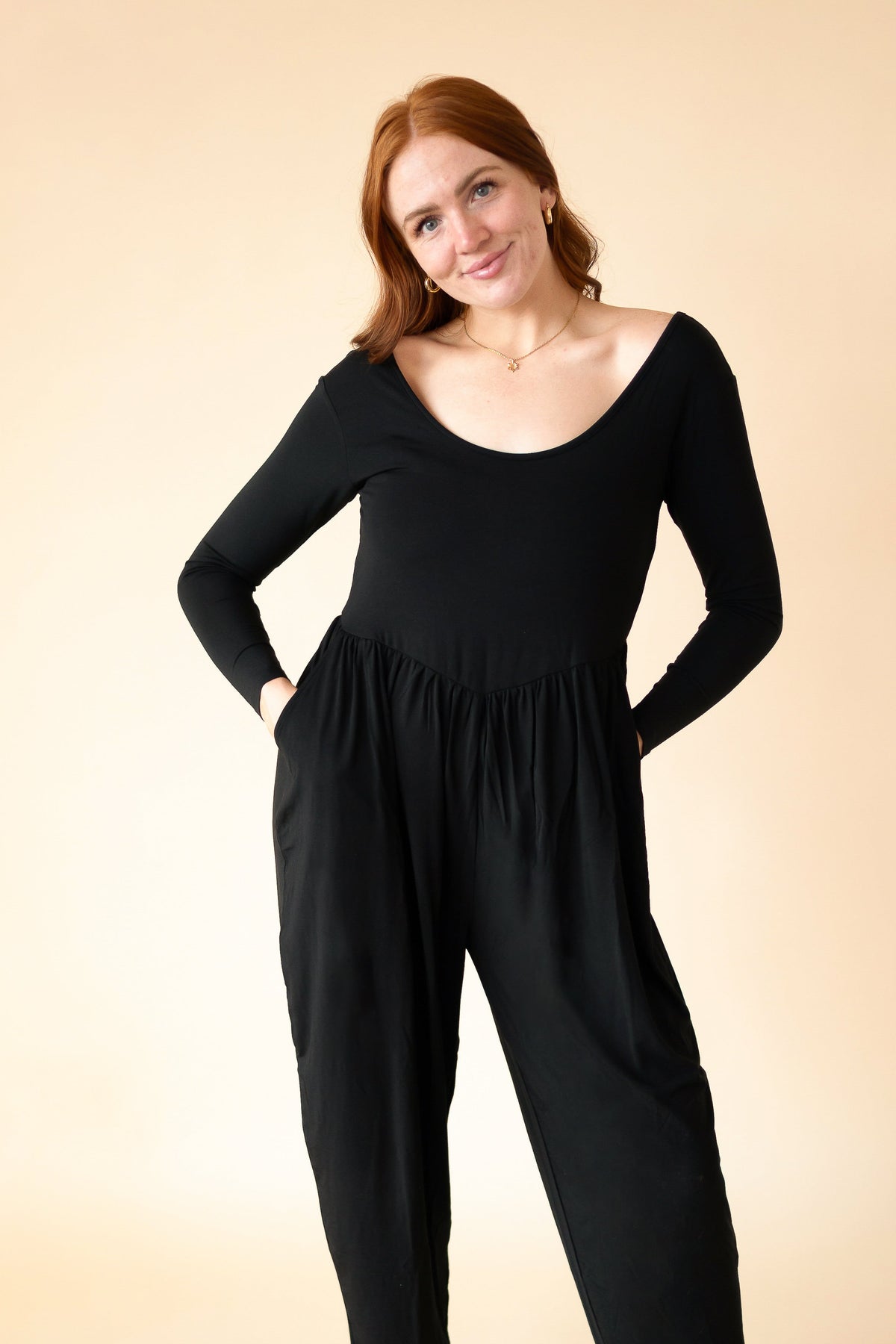 A woman wears a long-sleeve black Tencel Modal romper with a scoop neck and tapered legs.