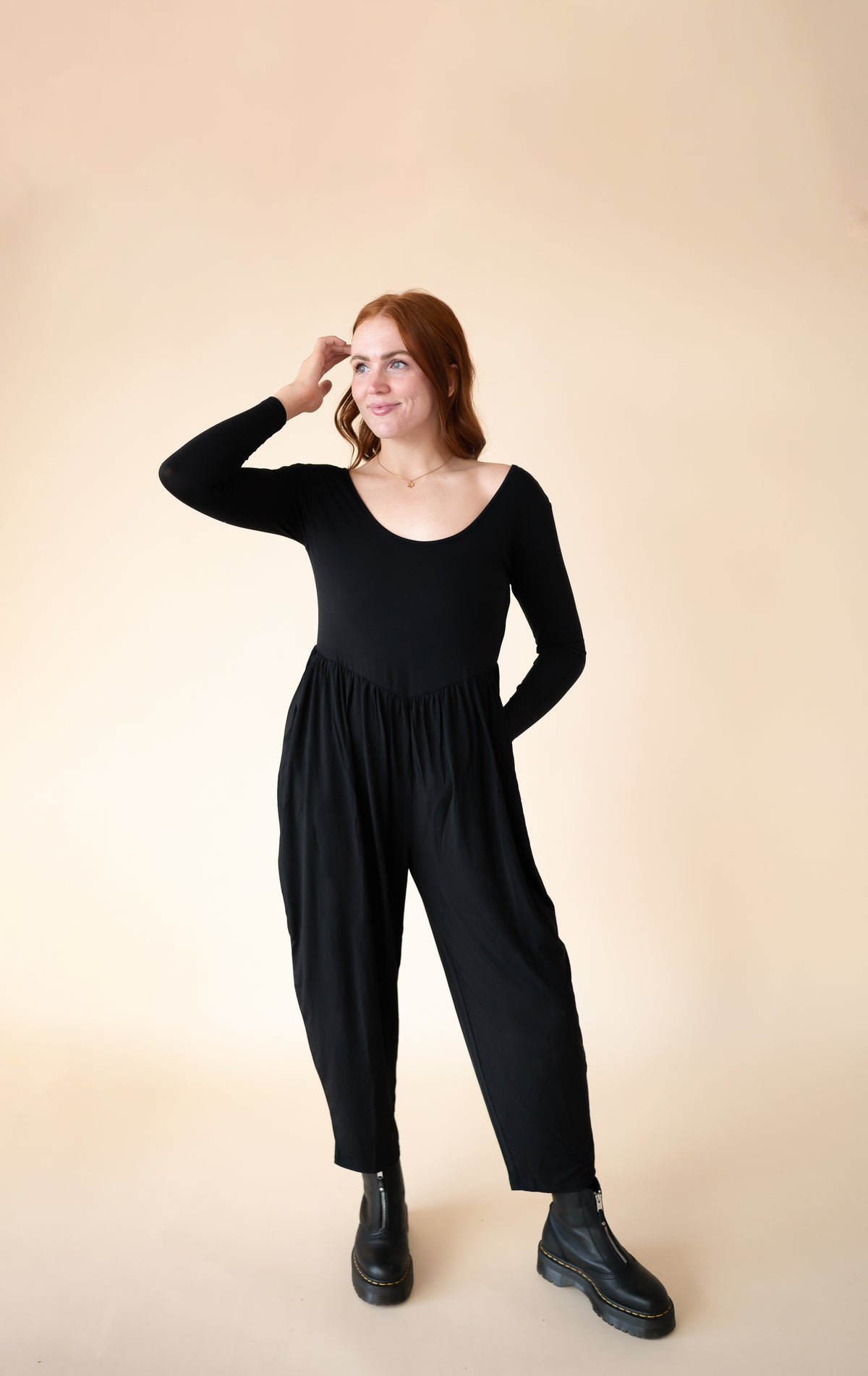 A woman wears a long-sleeve black Tencel Modal romper with a scoop neck and tapered legs.