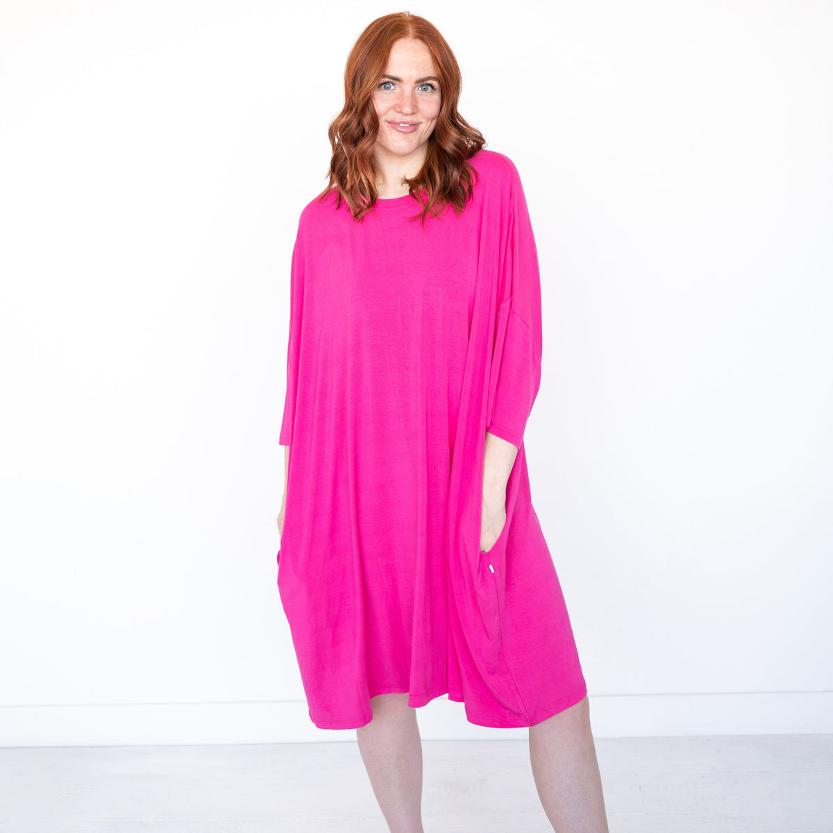 A woman with red hair wears a bright pink, oversized bamboo sleep tee with pockets.