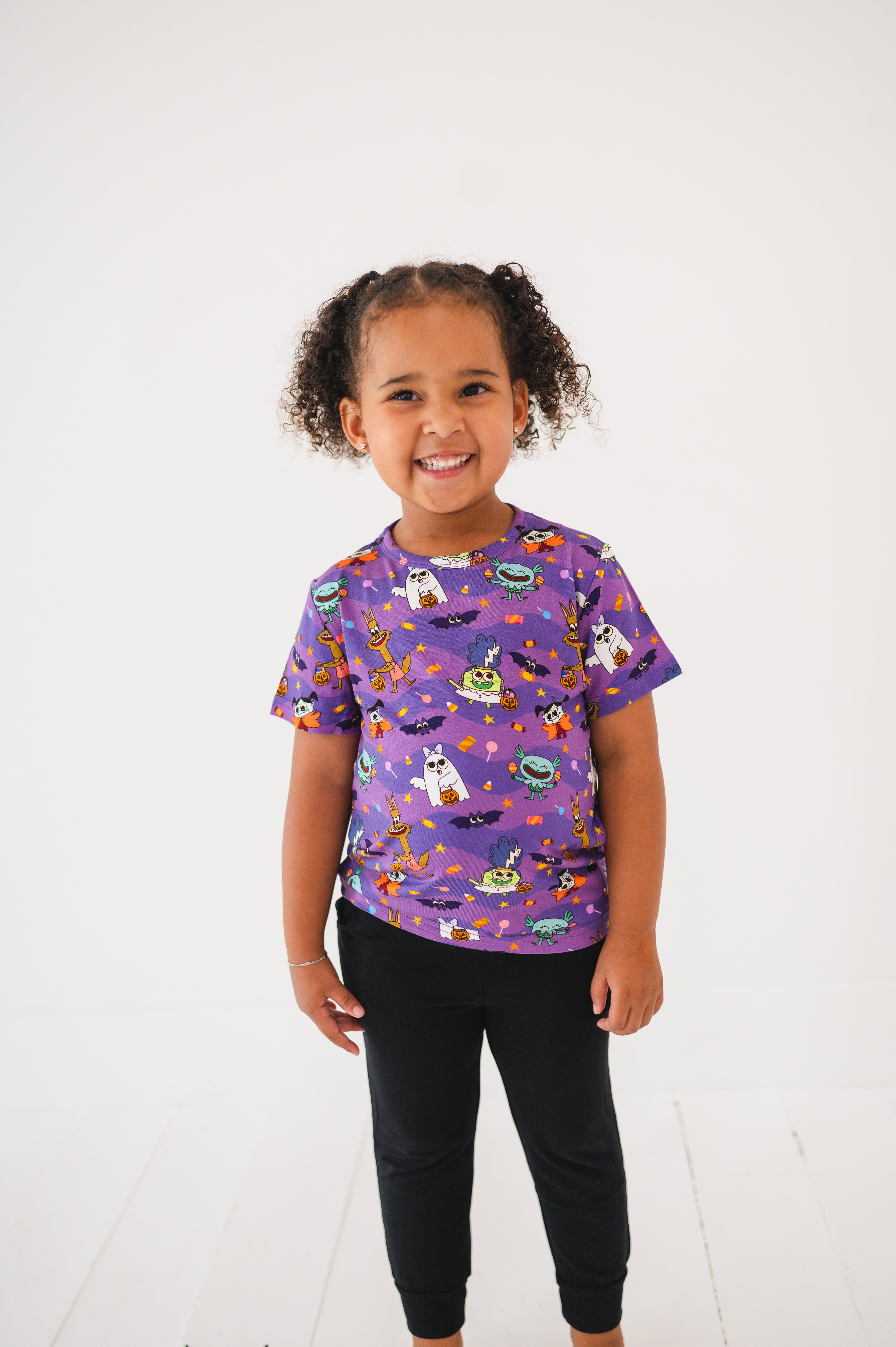 A young girl wears a purple t-shirt with a monster party print.