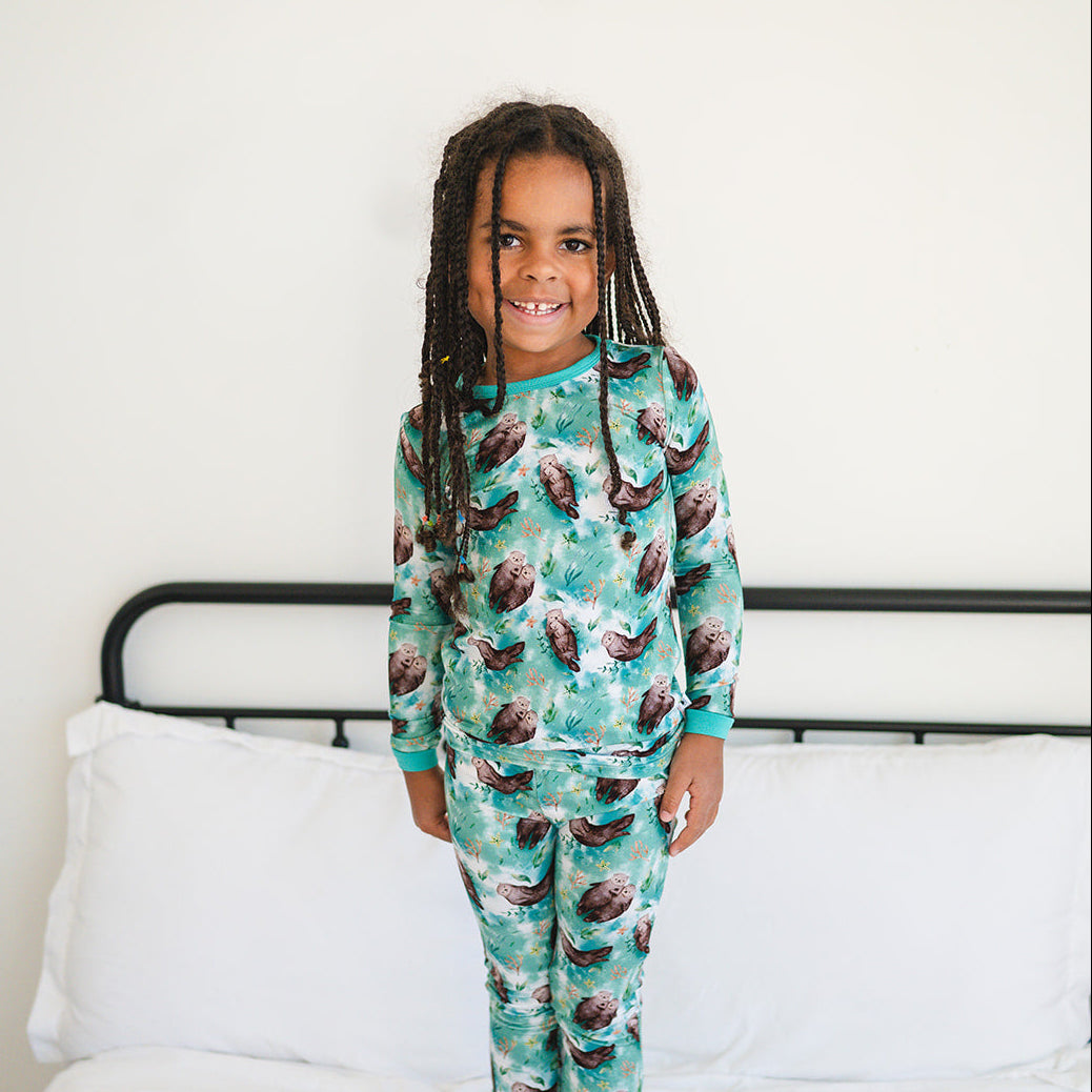 A young child smiles wearing a long-sleeved pajama set with an otter print.