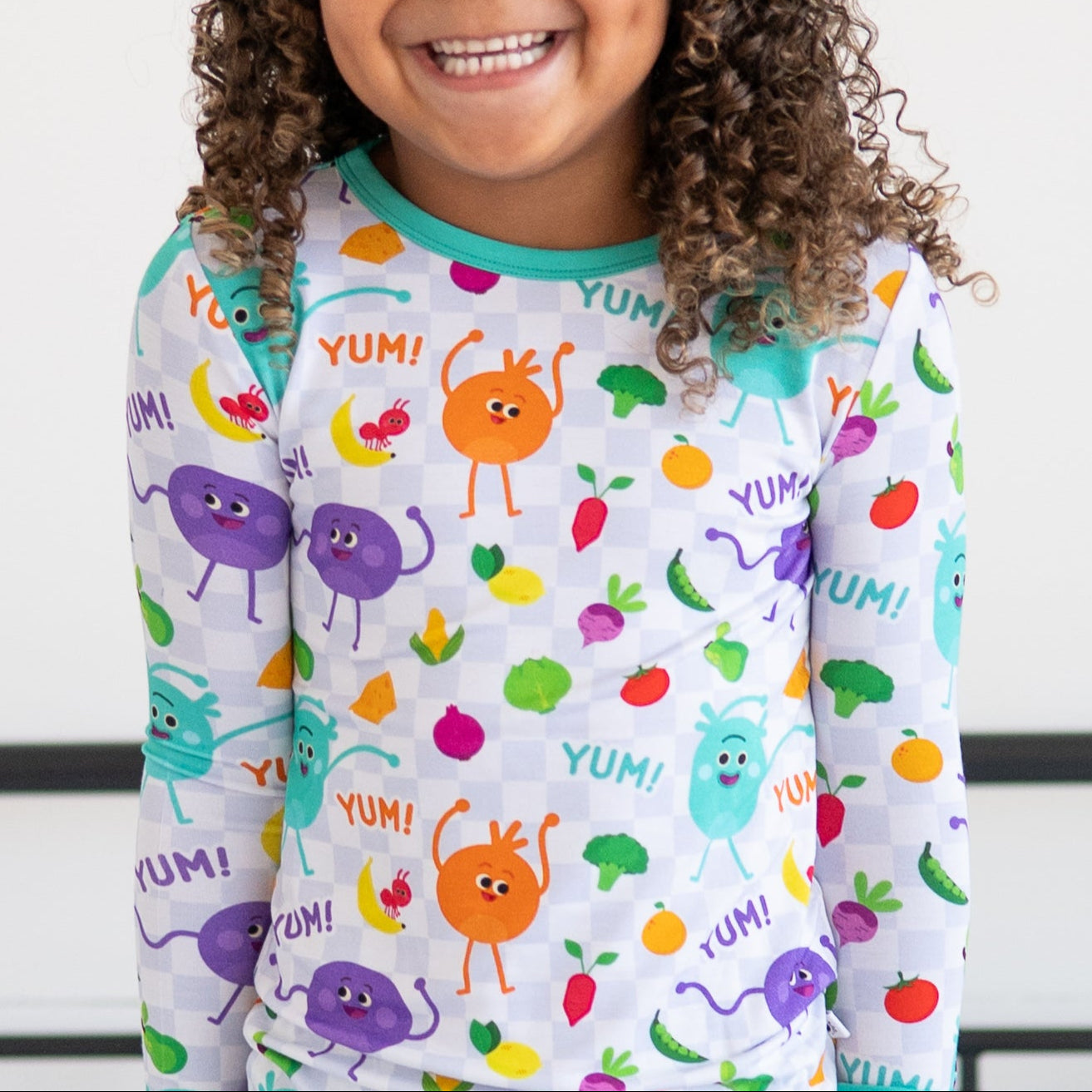 A child wears a long-sleeved pajama top with a checkerboard pattern and cartoon vegetables.