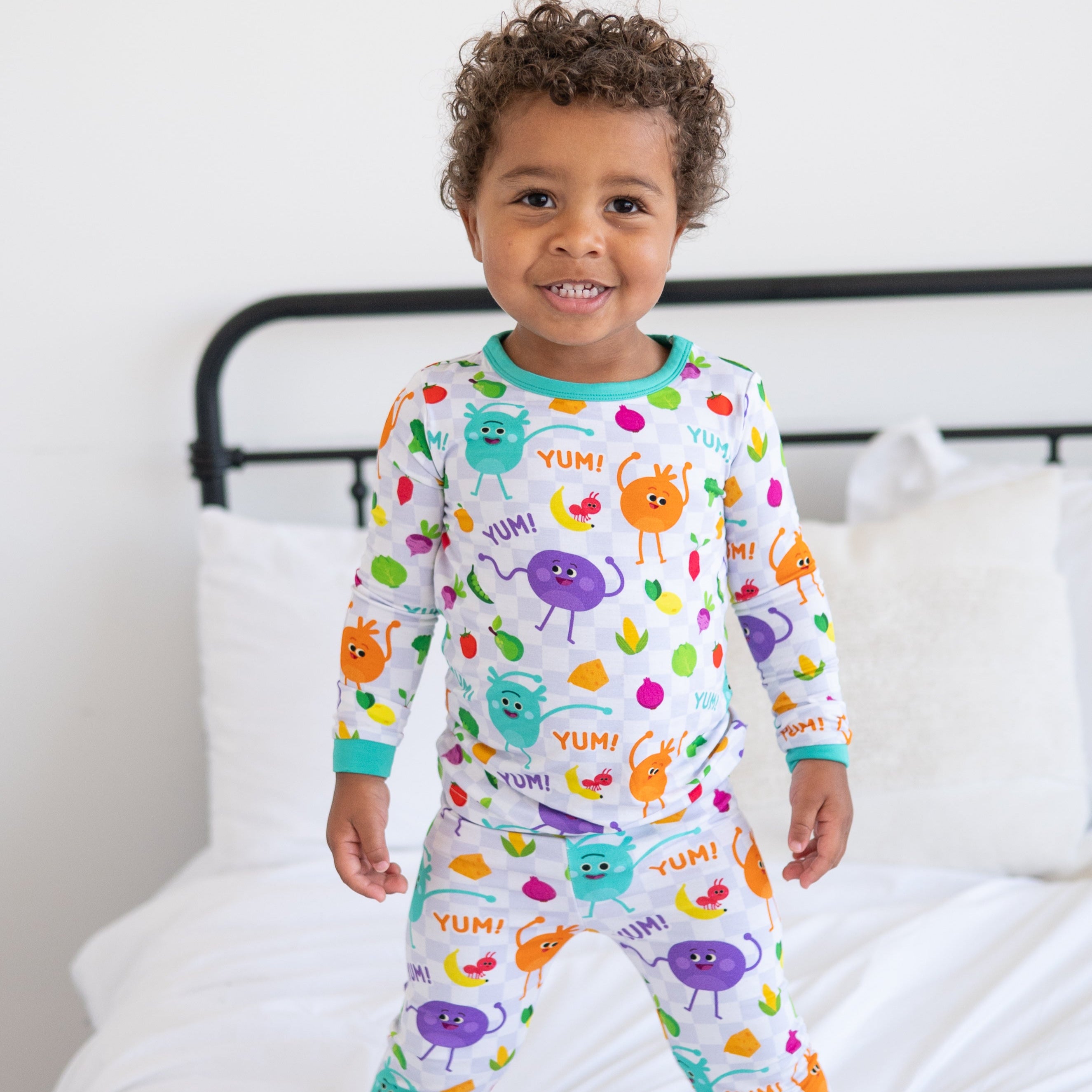 A young boy smiles while wearing white pajamas with a checkerboard pattern and colorful fruit and vegetable characters.