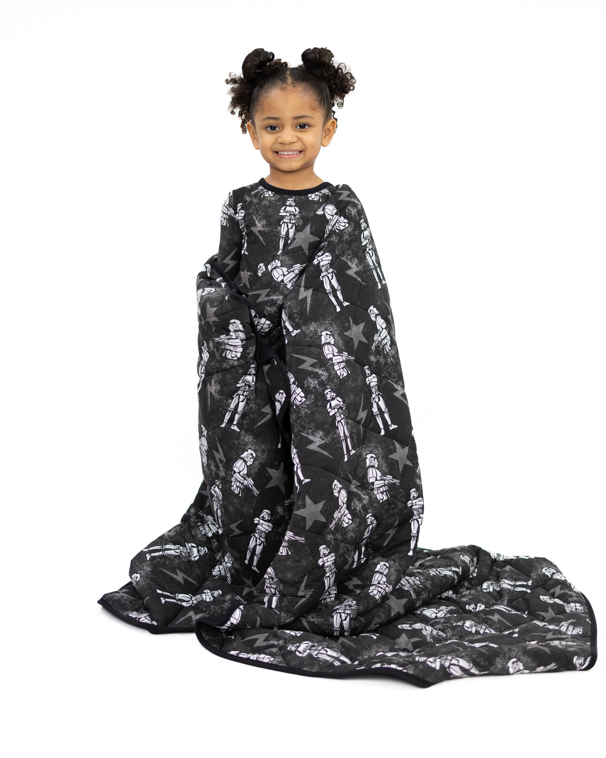 A young girl smiles while wrapped in a black blanket with a Star Wars Stormtrooper print.