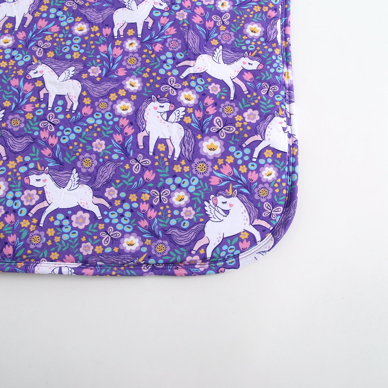 Purple blanket with a pattern of white unicorns and flowers.