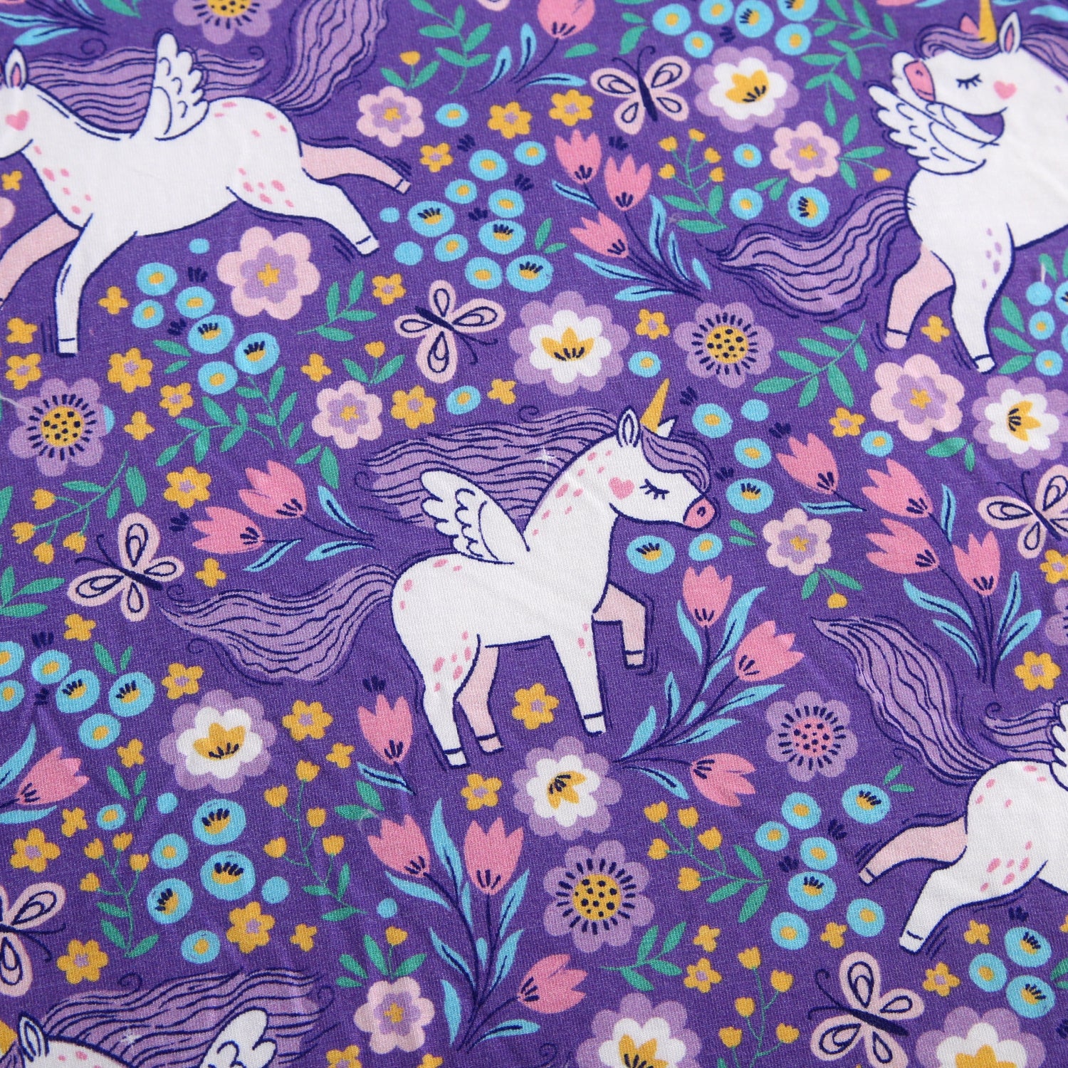 A purple fabric with a pattern of white unicorns and colorful flowers.