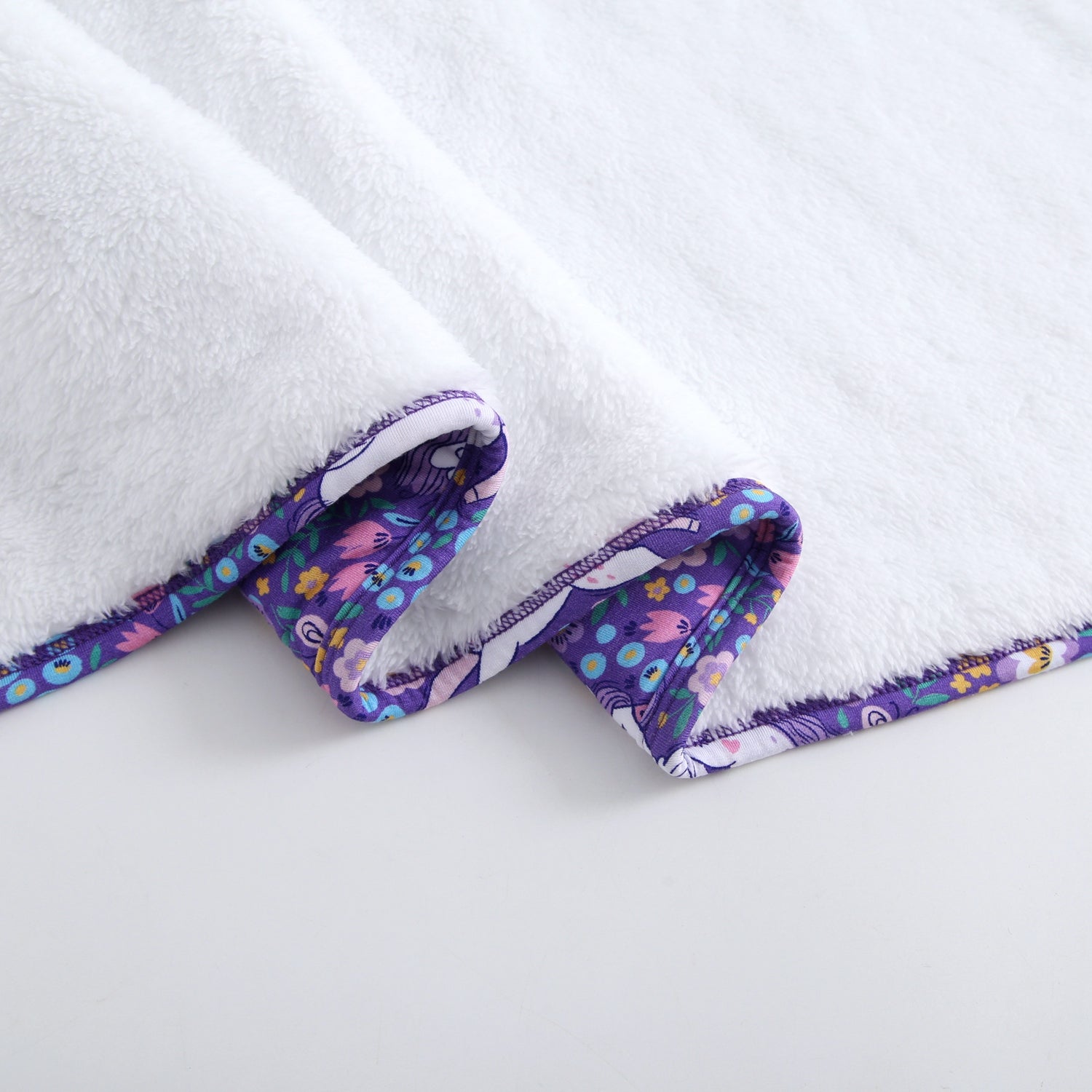 White plush blanket with a purple floral unicorn trim.