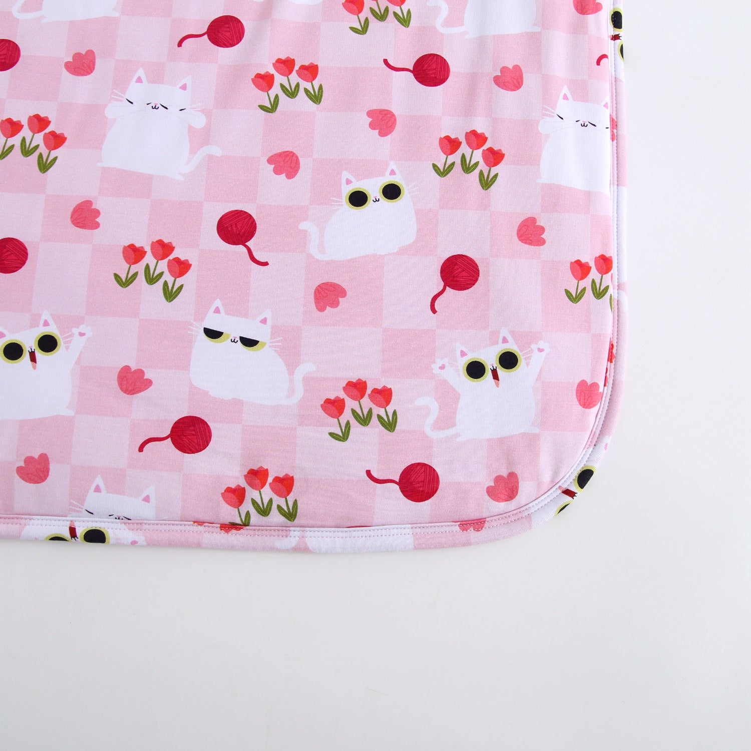 Pink blanket with a checkered pattern and cartoon cats, tulips, and yarn balls.
