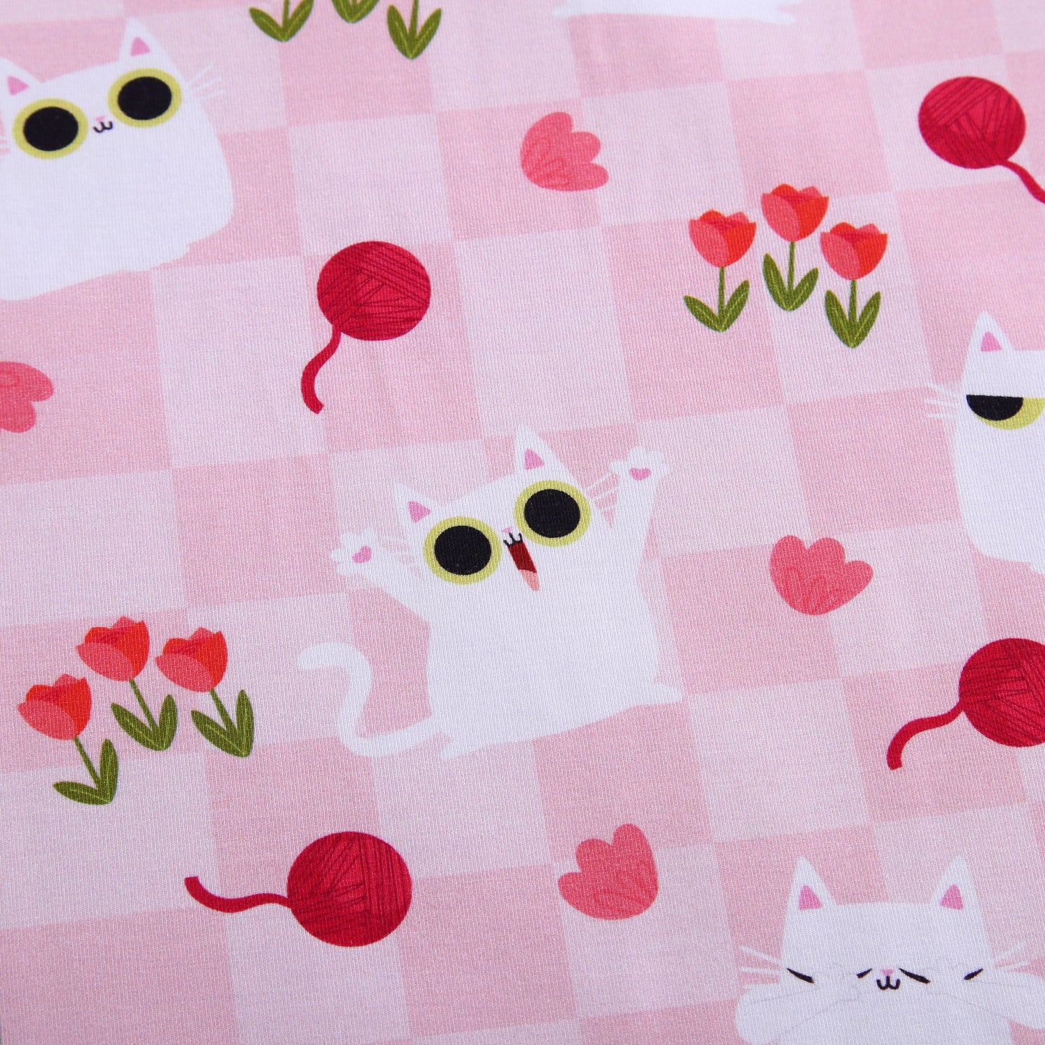 Pink fabric with a gingham pattern featuring white cartoon cats and red yarn balls.