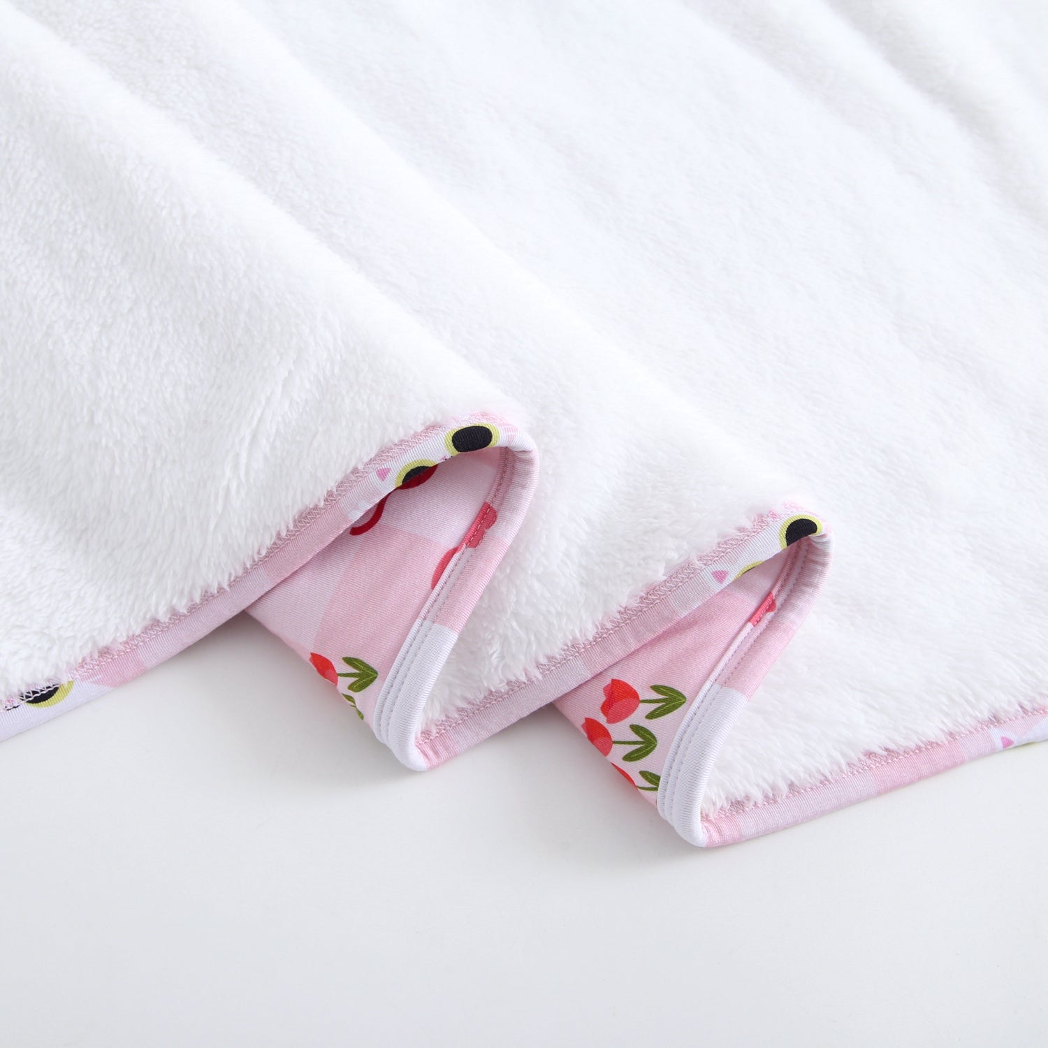 White plush blanket with a pink and white checkered trim featuring cartoon cats and red flowers.