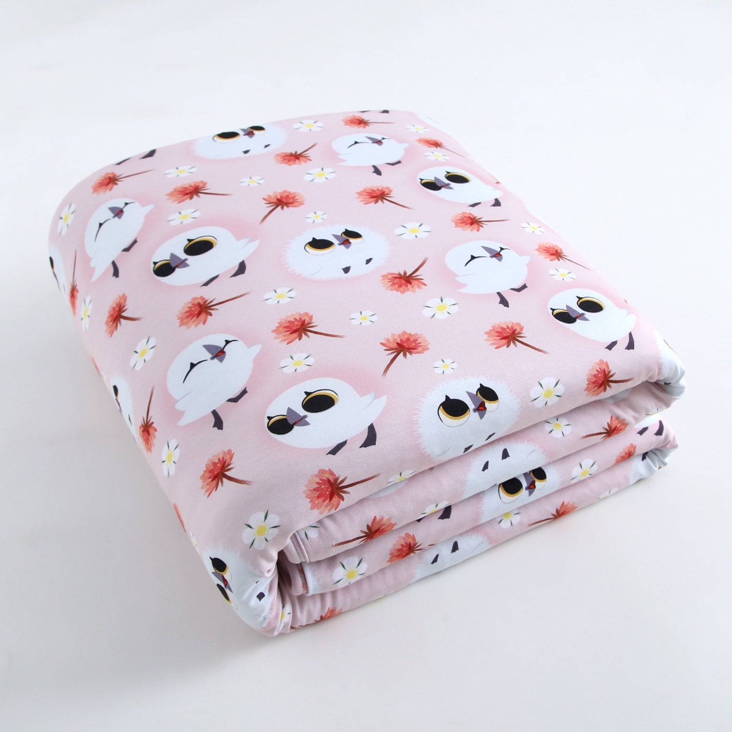 A pink blanket with a pattern of cartoon puffins and flowers.
