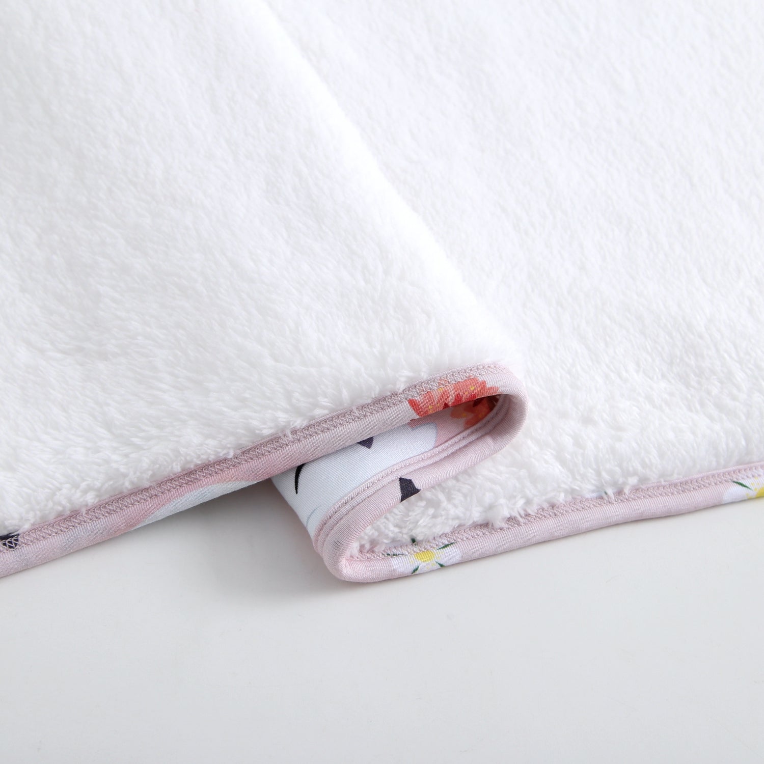 White plush blanket with a pink floral trim.