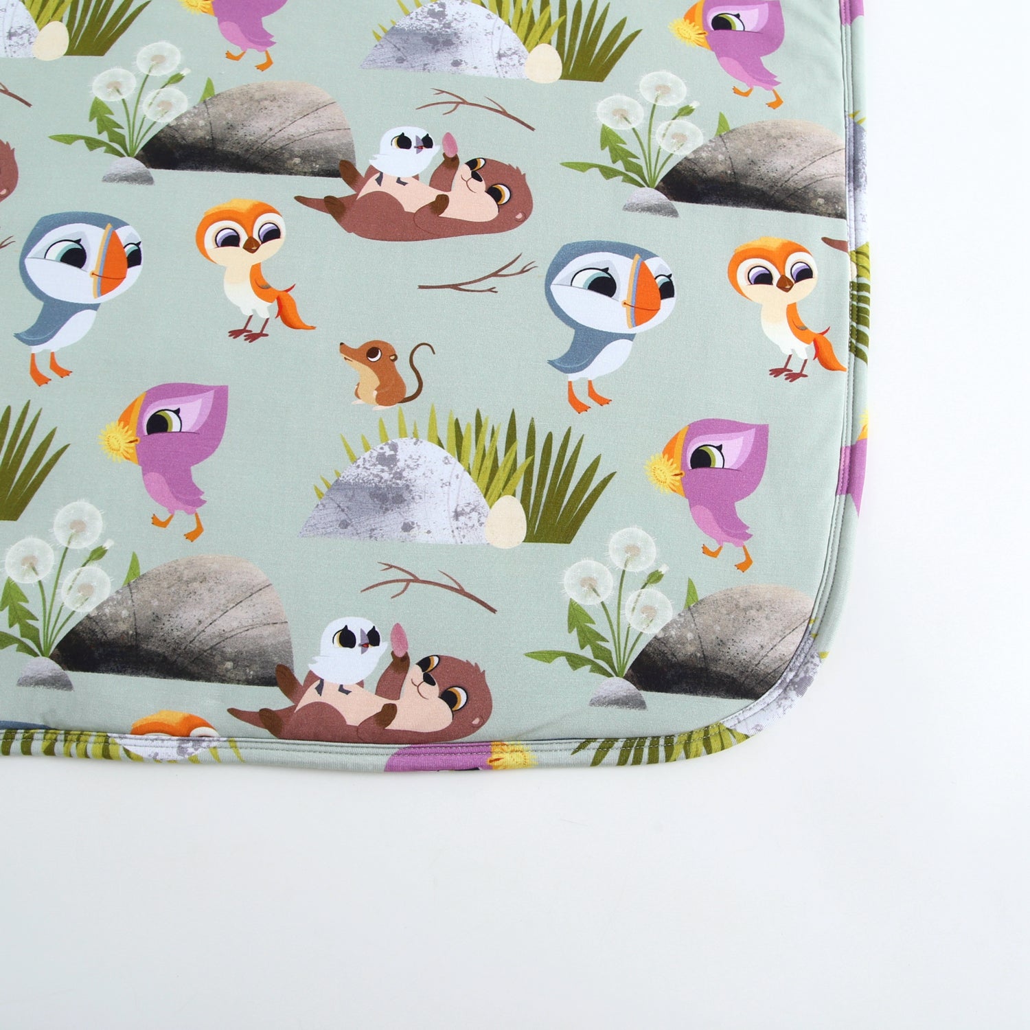 A light green blanket with a Puffin Rock pattern featuring puffins, otters, and mice.