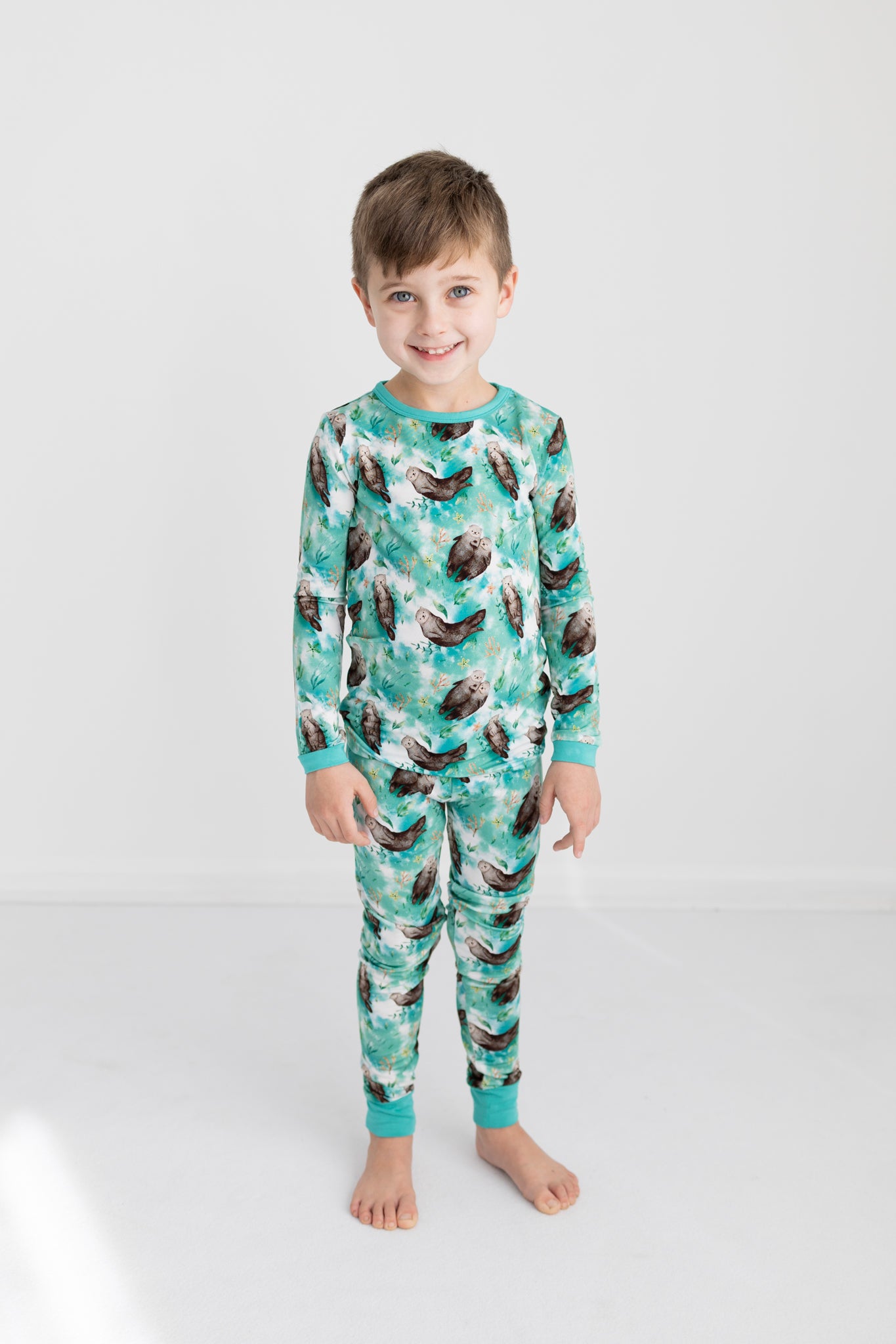 A young boy smiles wearing a long-sleeved pajama set with an otter print.
