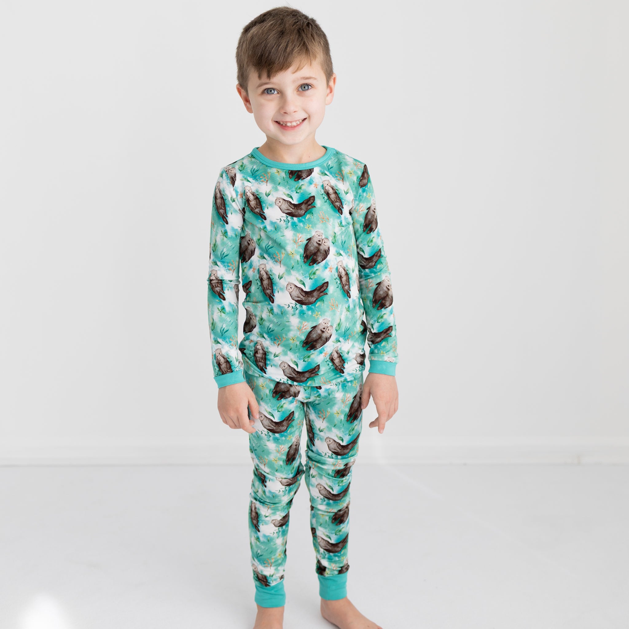 A young boy smiles wearing a long-sleeved pajama set with an otter print.