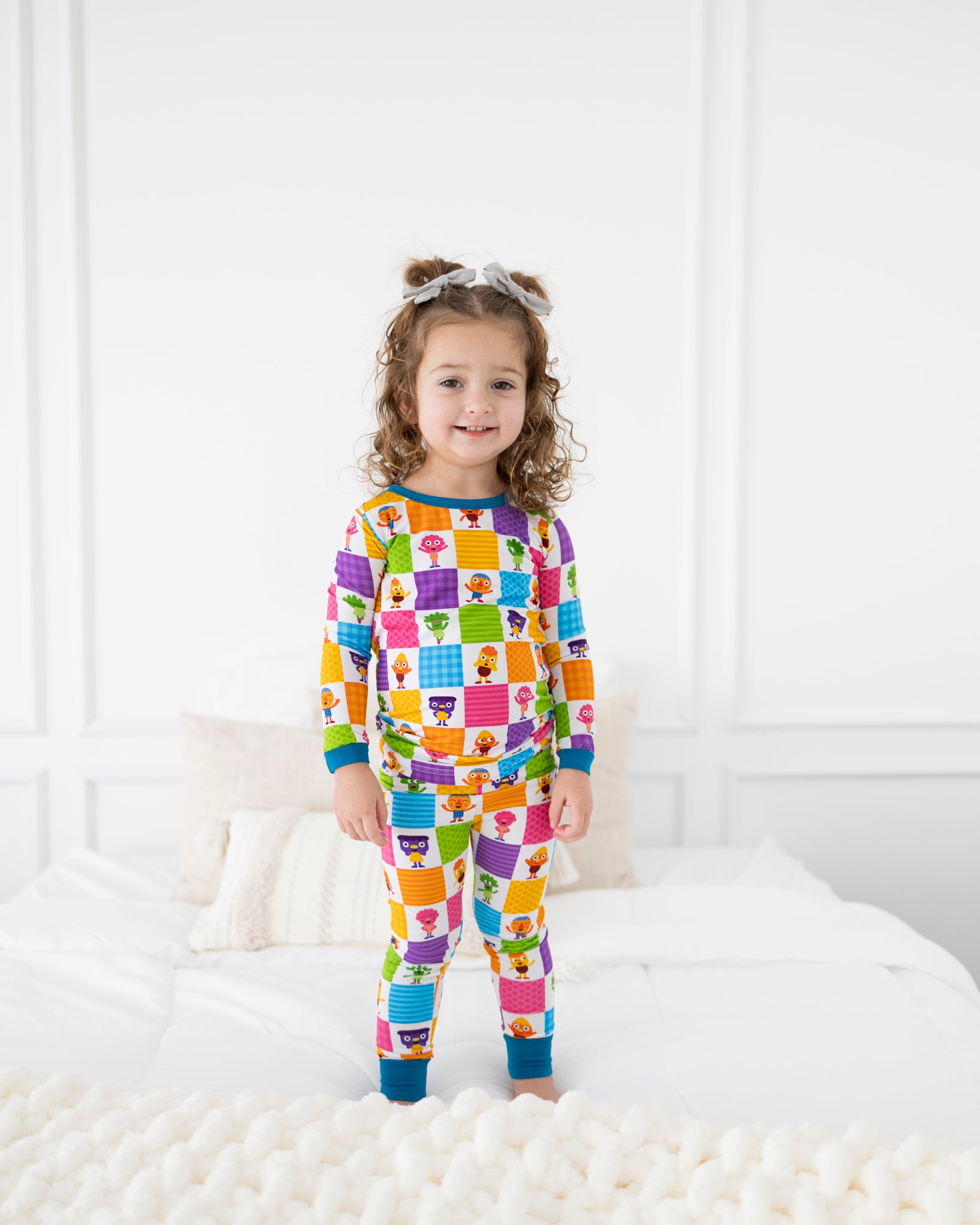 A young girl wears colorful pajamas with a checkered pattern of cartoon characters.