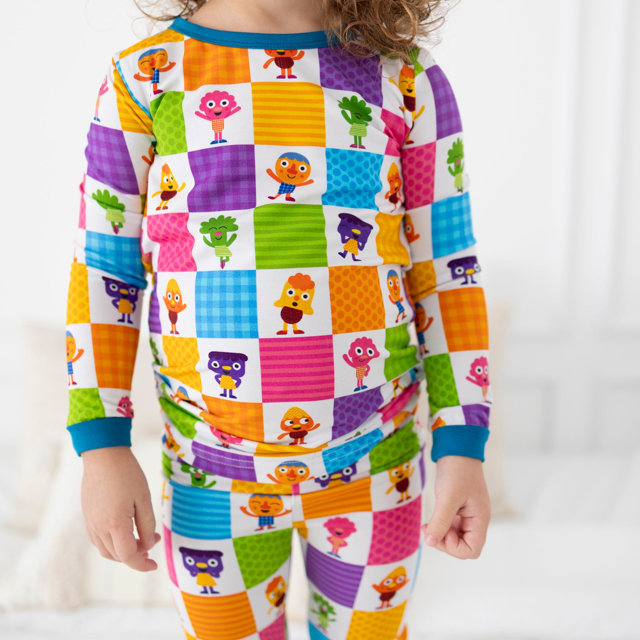 A child wears colorful long-sleeved pajamas with a checkerboard pattern featuring cartoon characters.