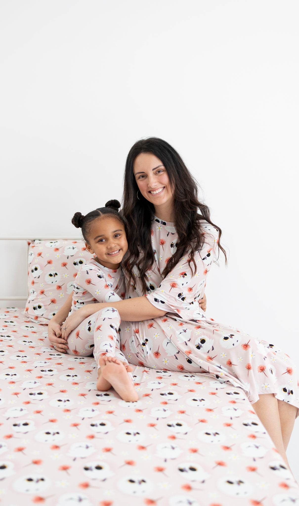 A woman and child in matching pink Puffin Rock pajamas sit on a bed.