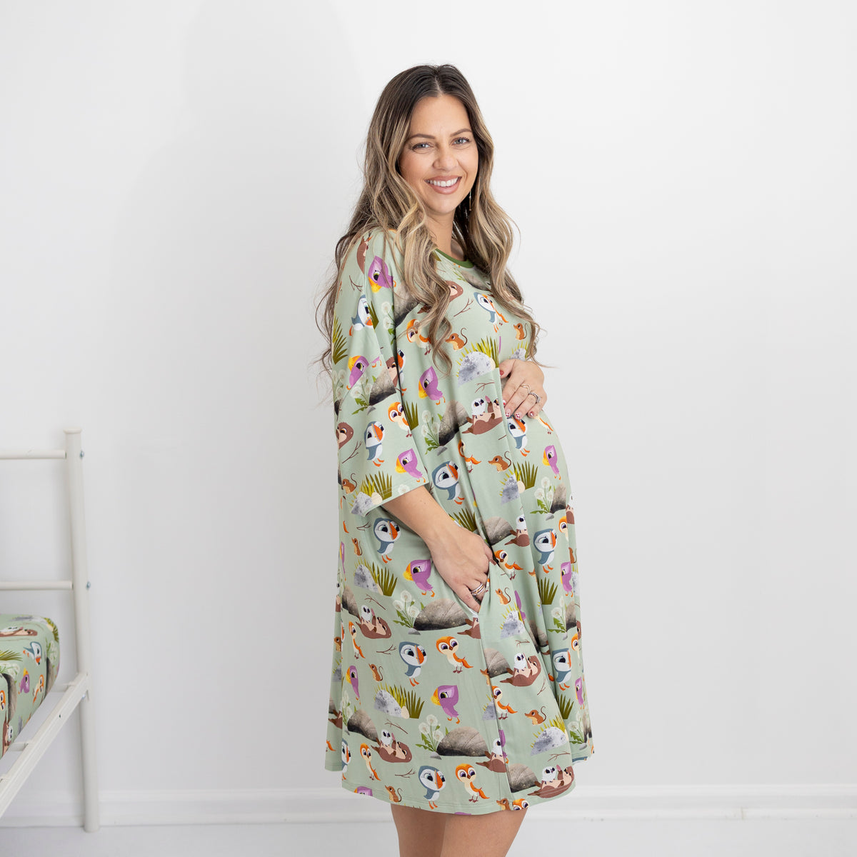 A pregnant woman smiles wearing a light green sleep tee with a puffin print.