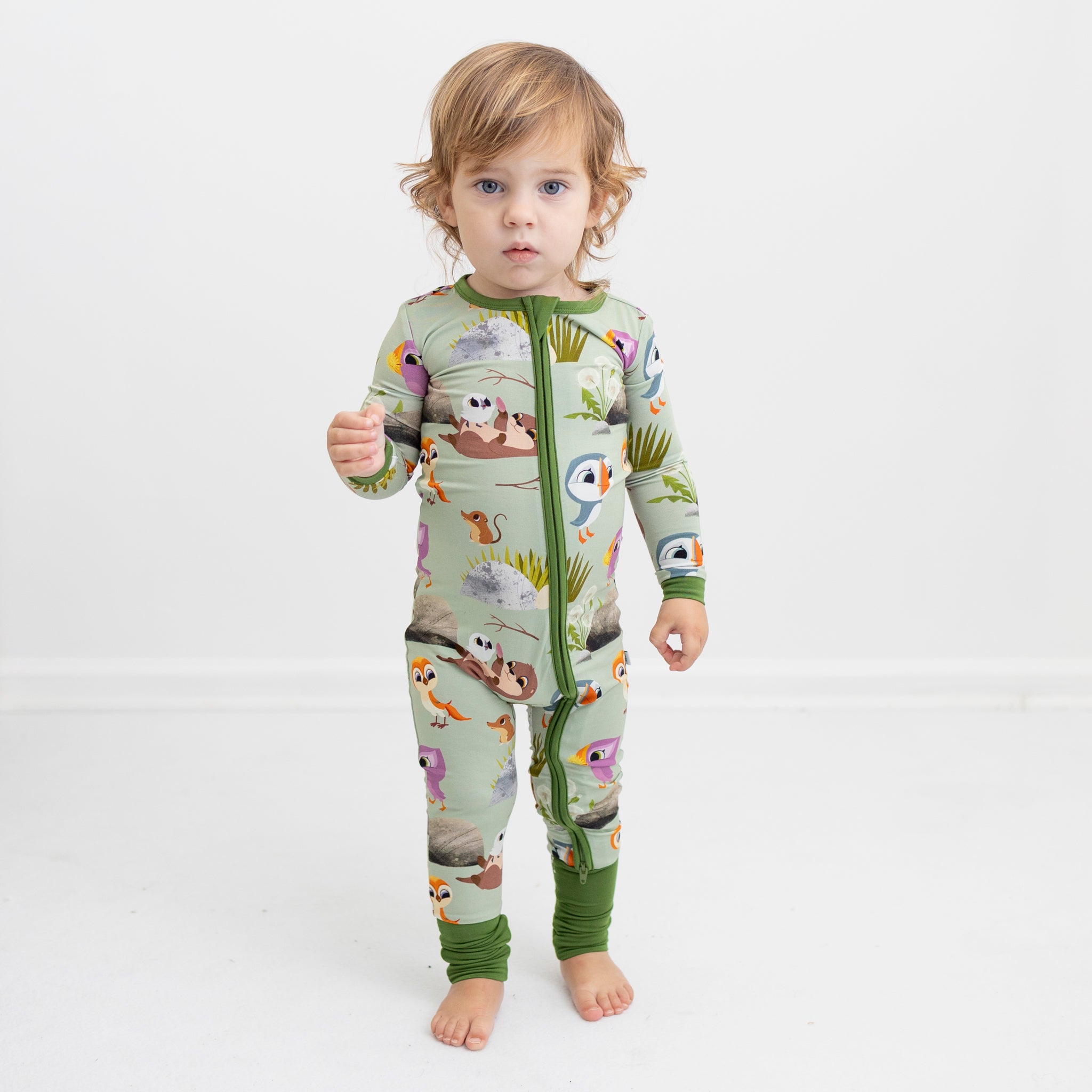 A toddler wears a light green pajama set with a Puffin Rock print.