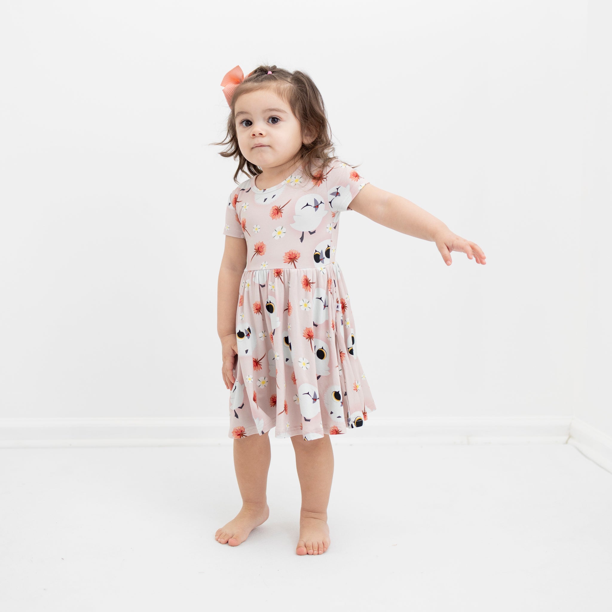 A young girl wears a pink Tencel Modal dress with a puffin print.