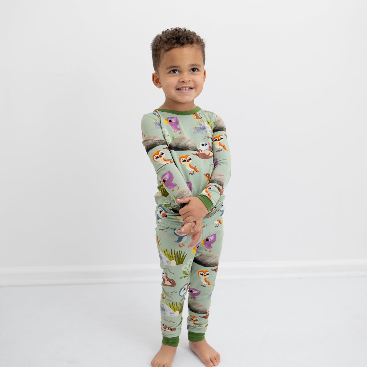 A young boy wears a light green pajama set with a Puffin Rock print.