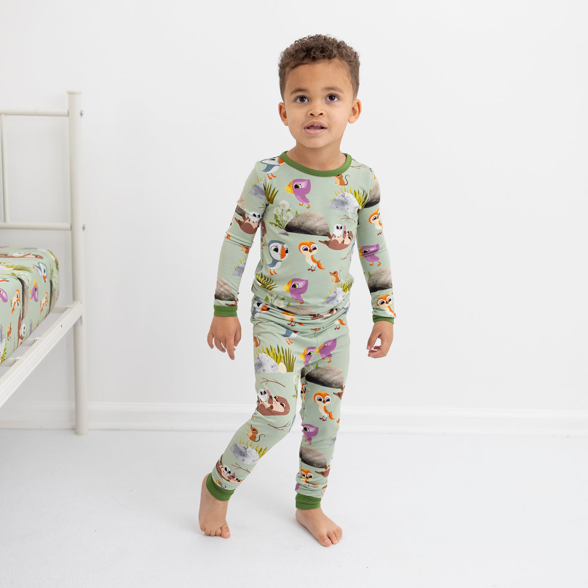 A young boy stands in a light green pajama set with a Puffin Rock print.