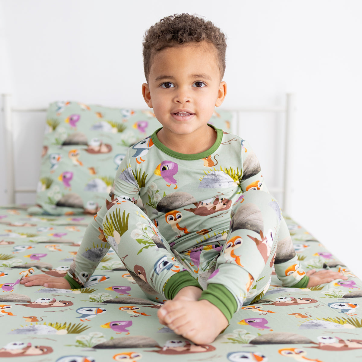 A young boy in Puffin Rock themed pajamas sits on a bed with a matching pillow.