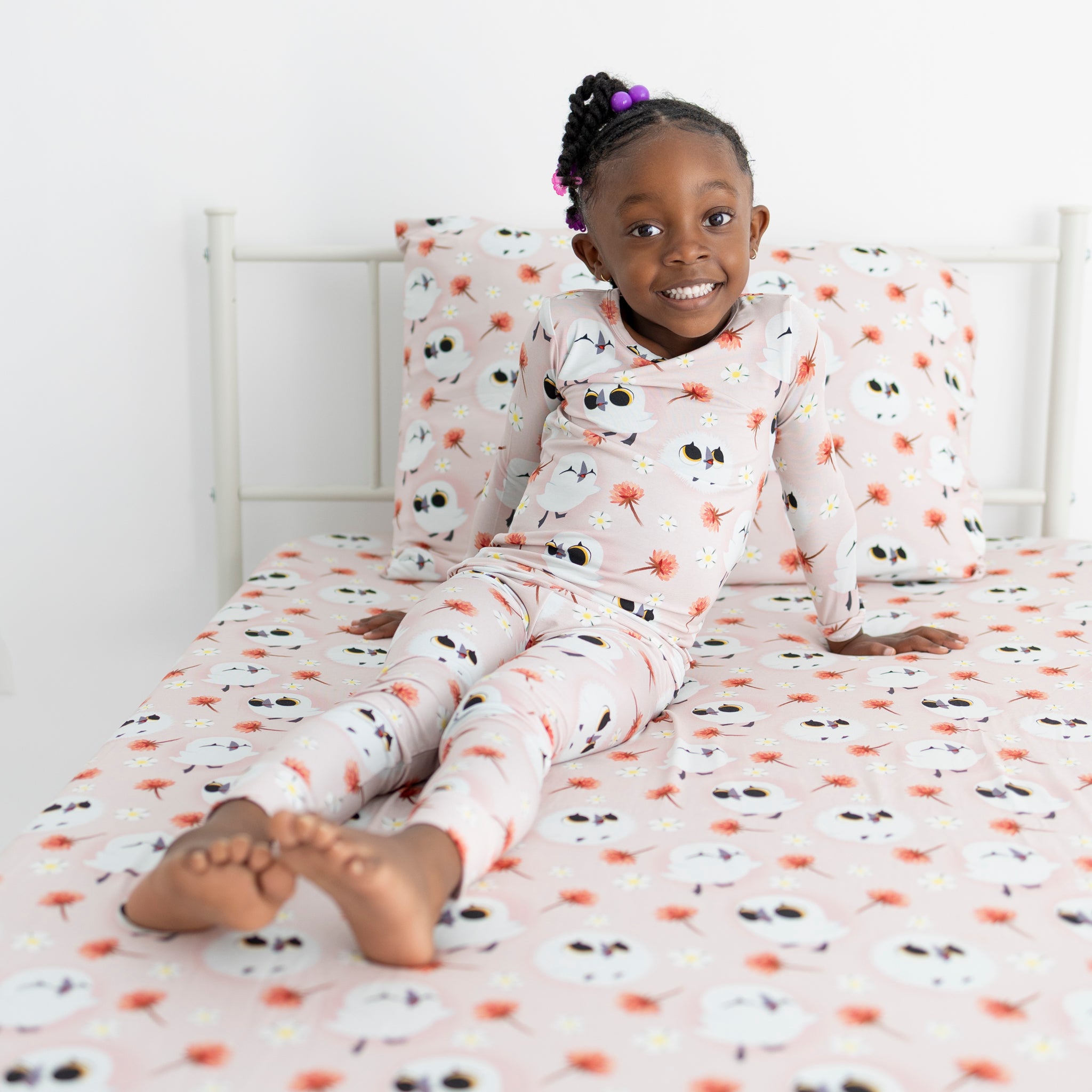 A young girl in pink owl pajamas sits on a bed with matching sheets.