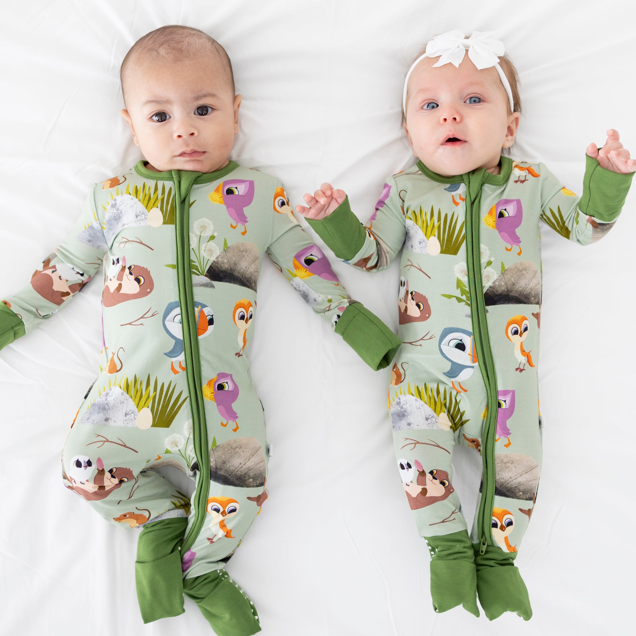 Two babies in light green pajamas with a Puffin Rock print.