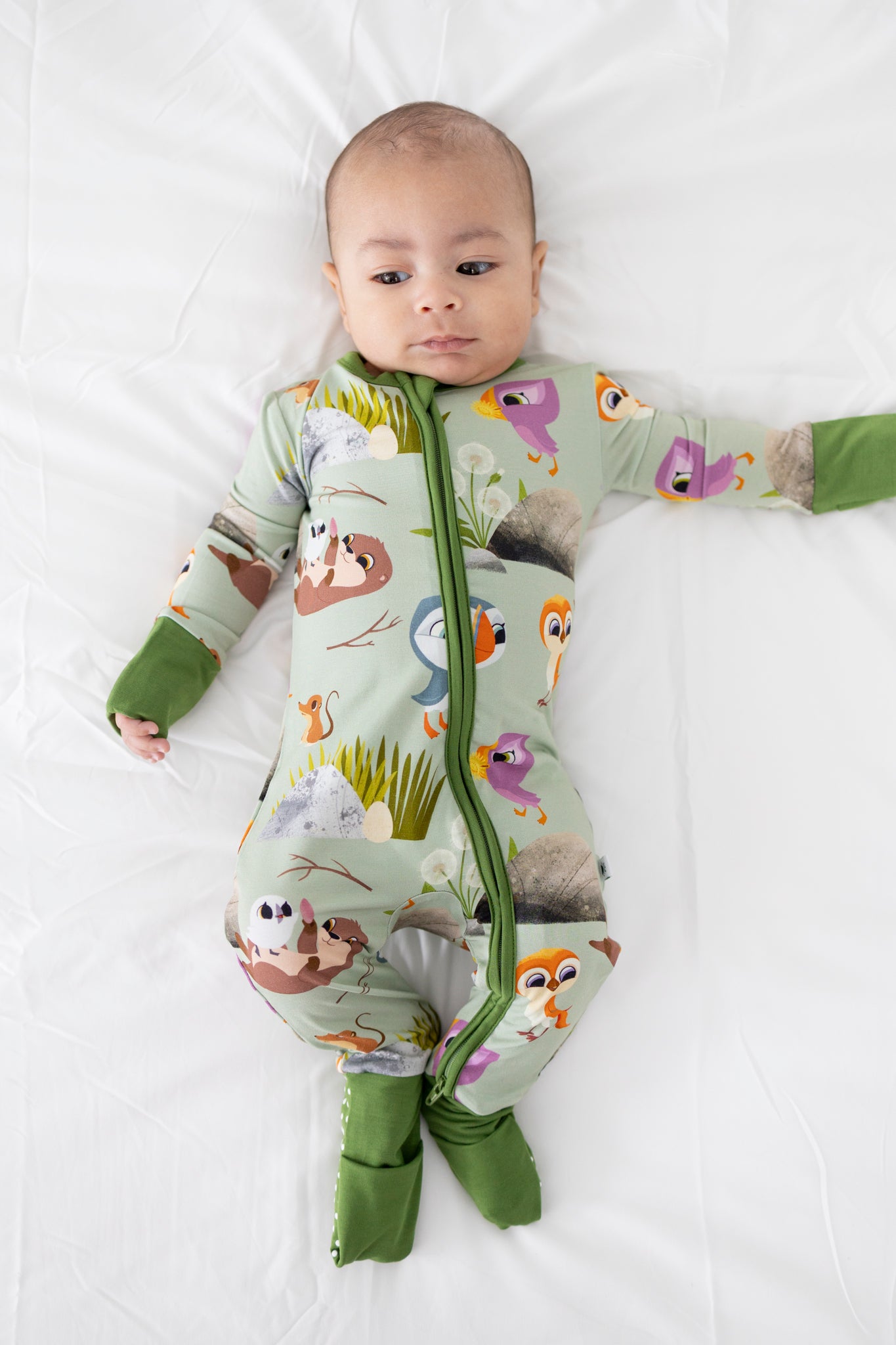 Baby in a light green Puffin Rock™ Tencel™ Modal zip pajama with bird and animal prints.