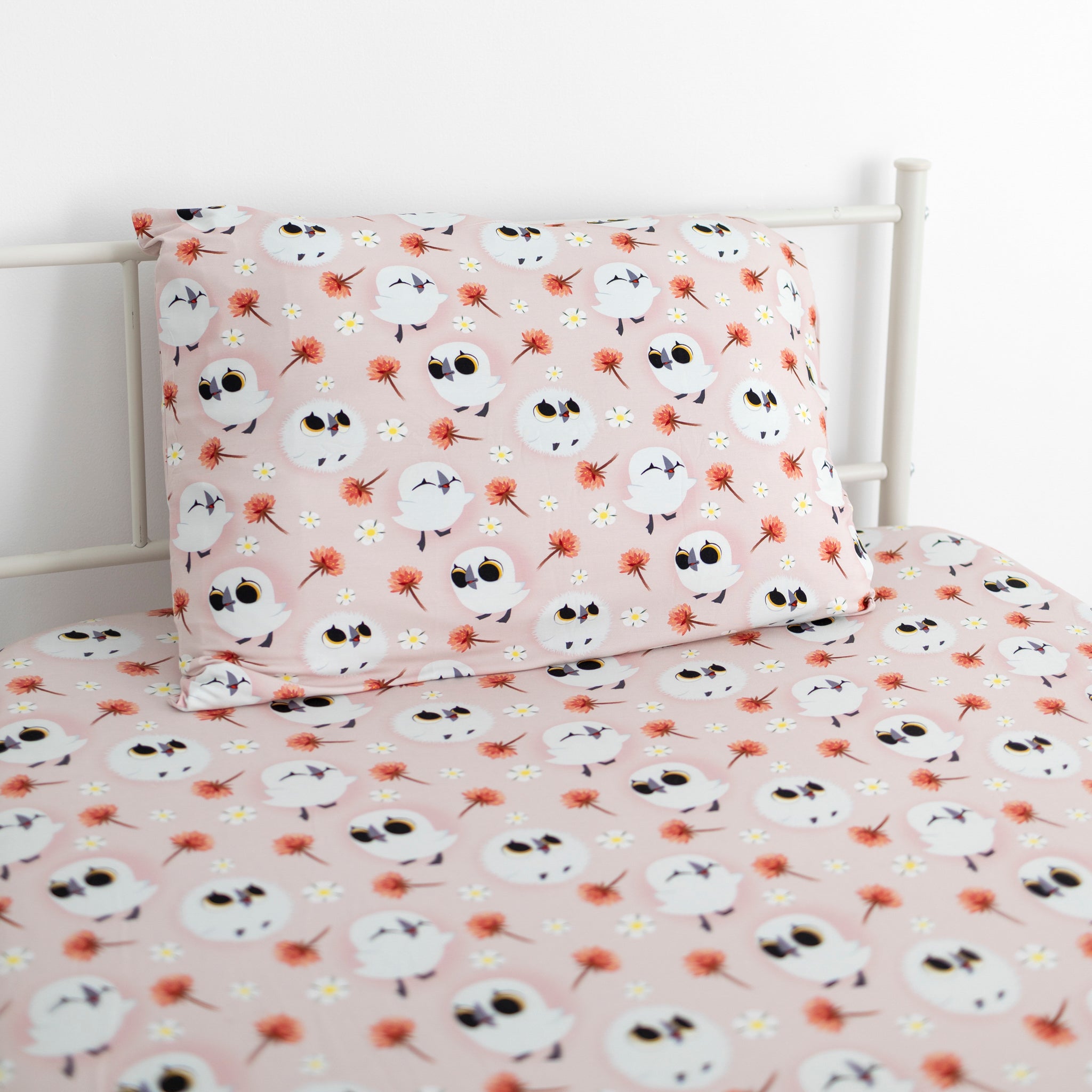 Twin sheet and pillowcase set with a pink background and a pattern of cartoon puffins and flowers.