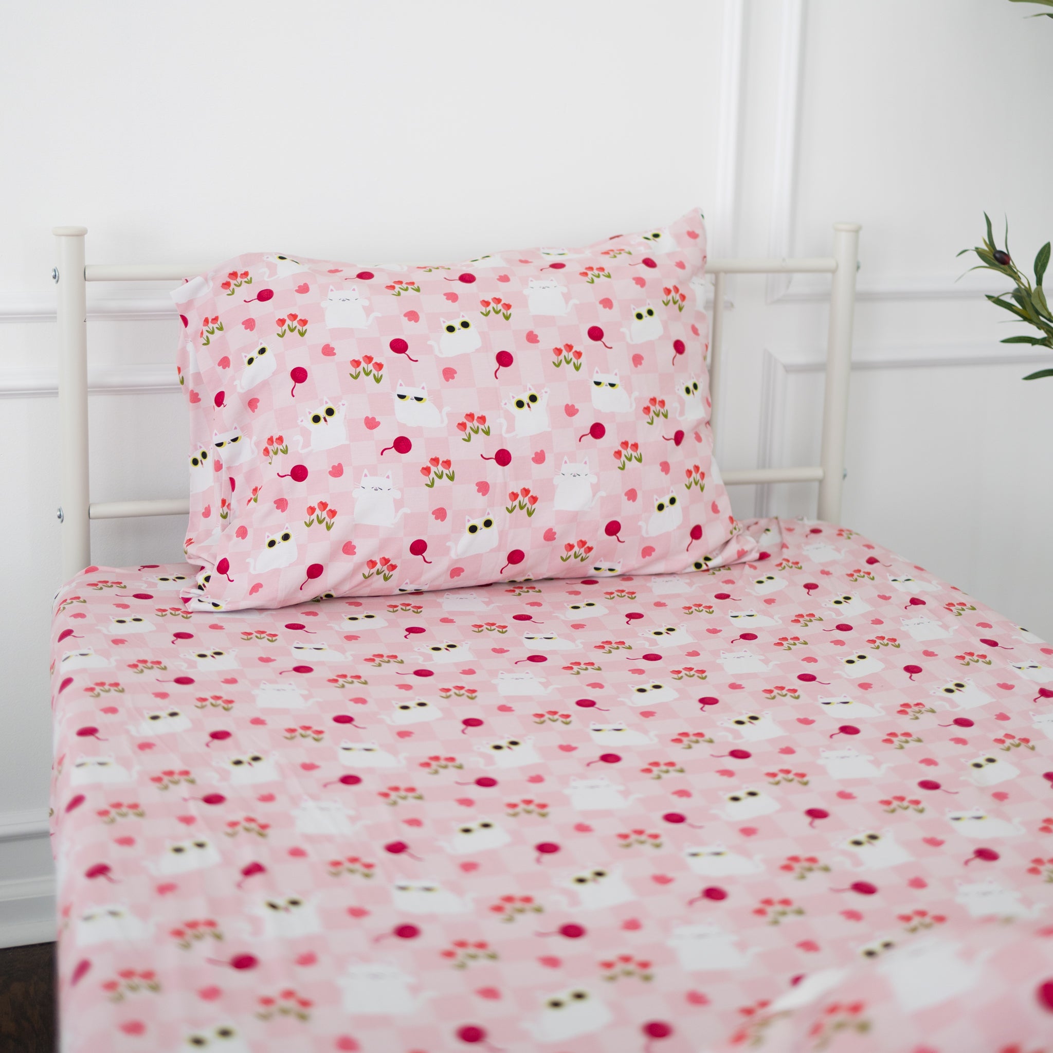 A twin sheet and pillowcase set featuring a pink checkered pattern with white cats and tulips.