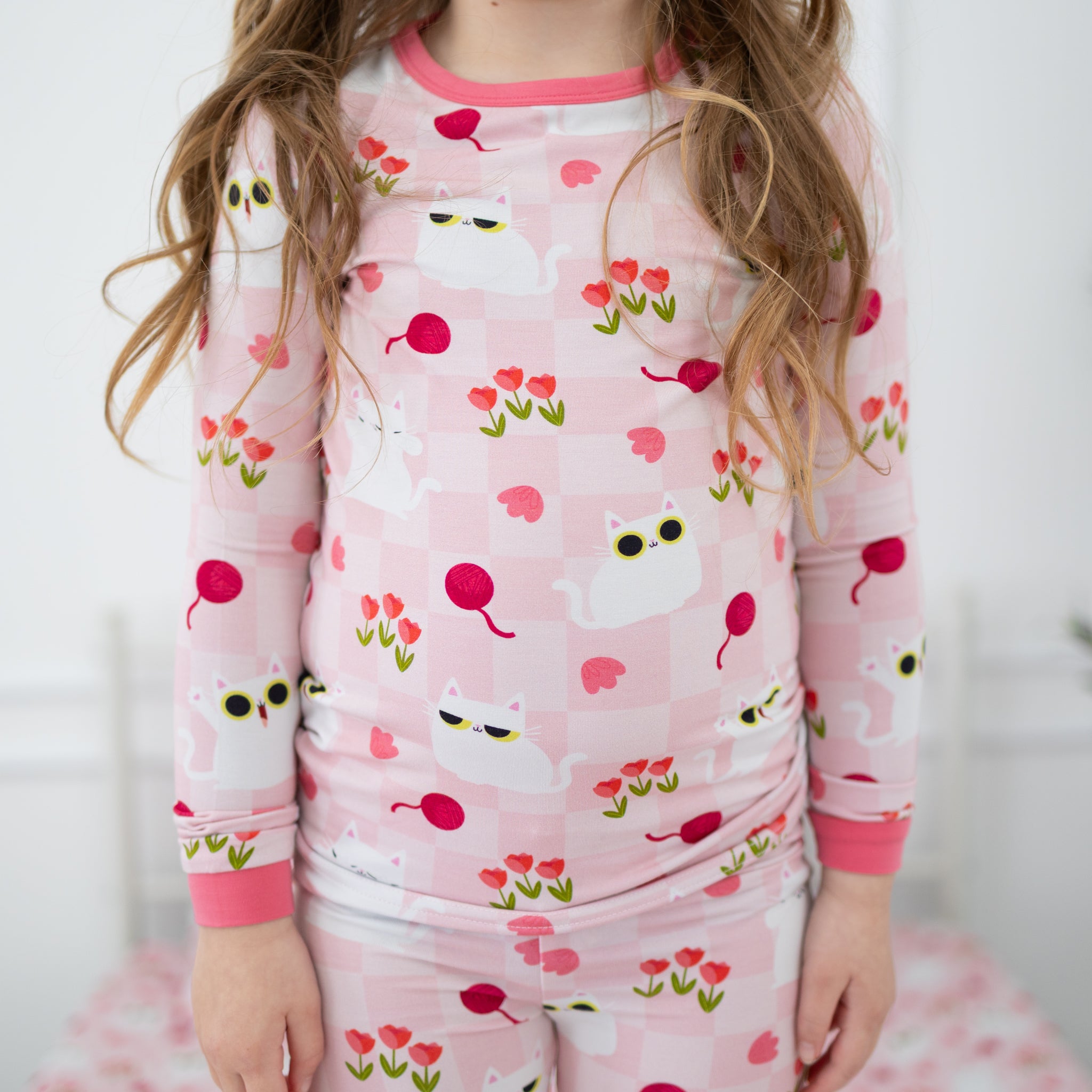 A child wears a pink and white checkered pajama set featuring a peek-a-boo cat and tulip print.