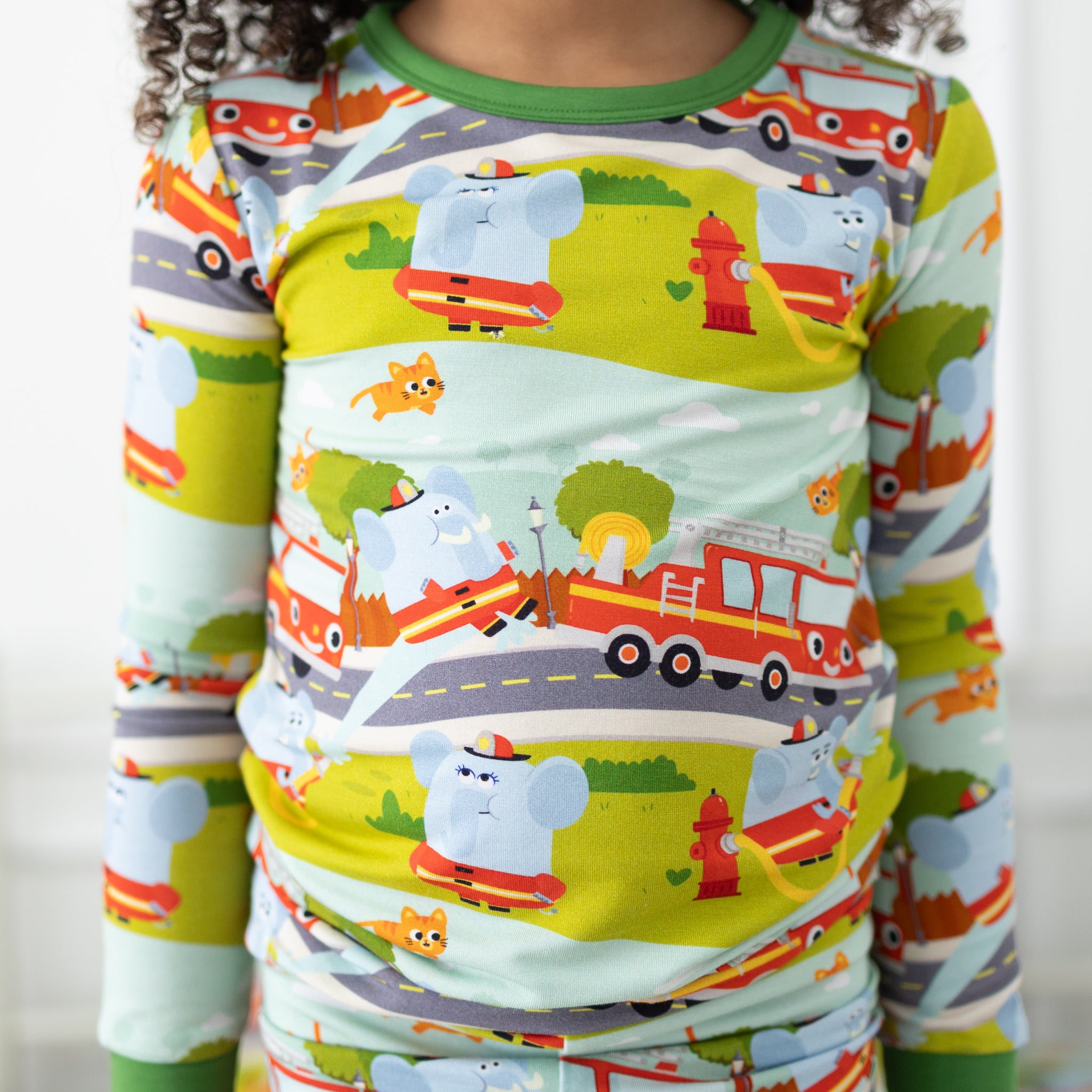 A child wears a long-sleeve pajama set featuring a light blue elephant and firetruck print.