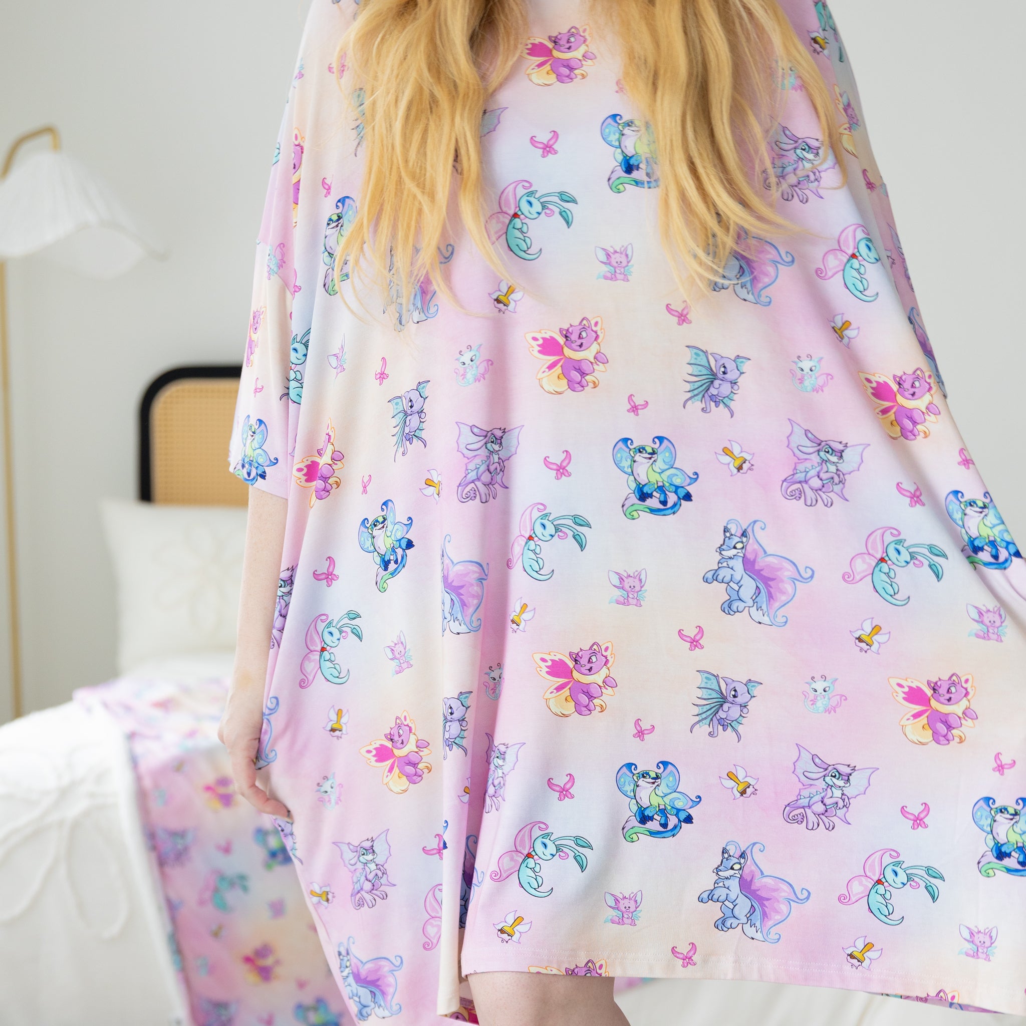 A person wears a pink and orange tie-dye sleep tee featuring a repeating Neopets Faerie pattern.