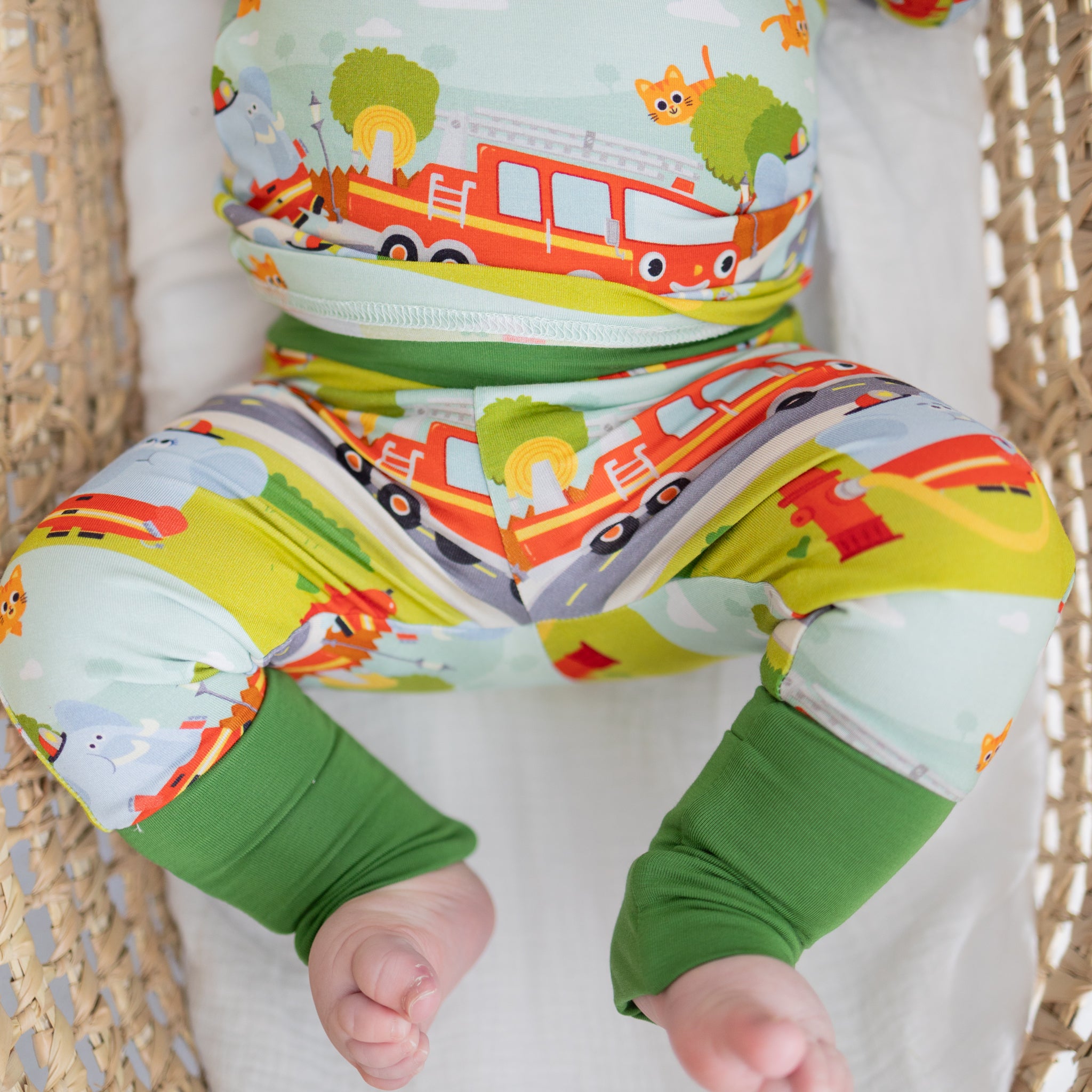A baby wears a light blue pajama set featuring a colorful firetruck and animal print.