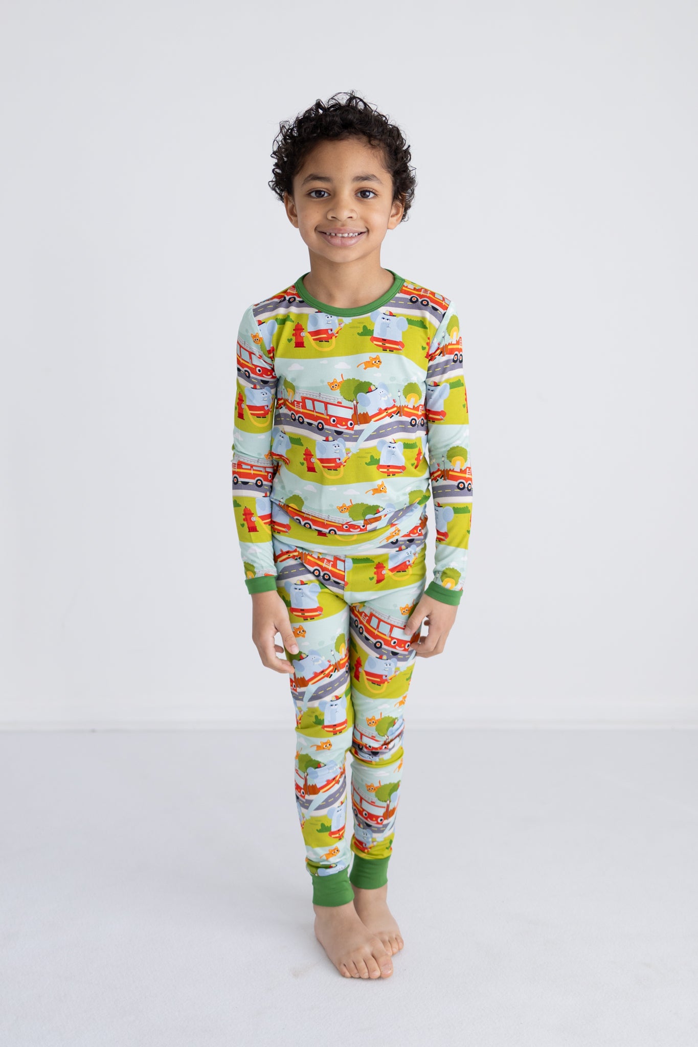 A child wears a long-sleeve pajama set featuring a colorful firetruck and animal print.