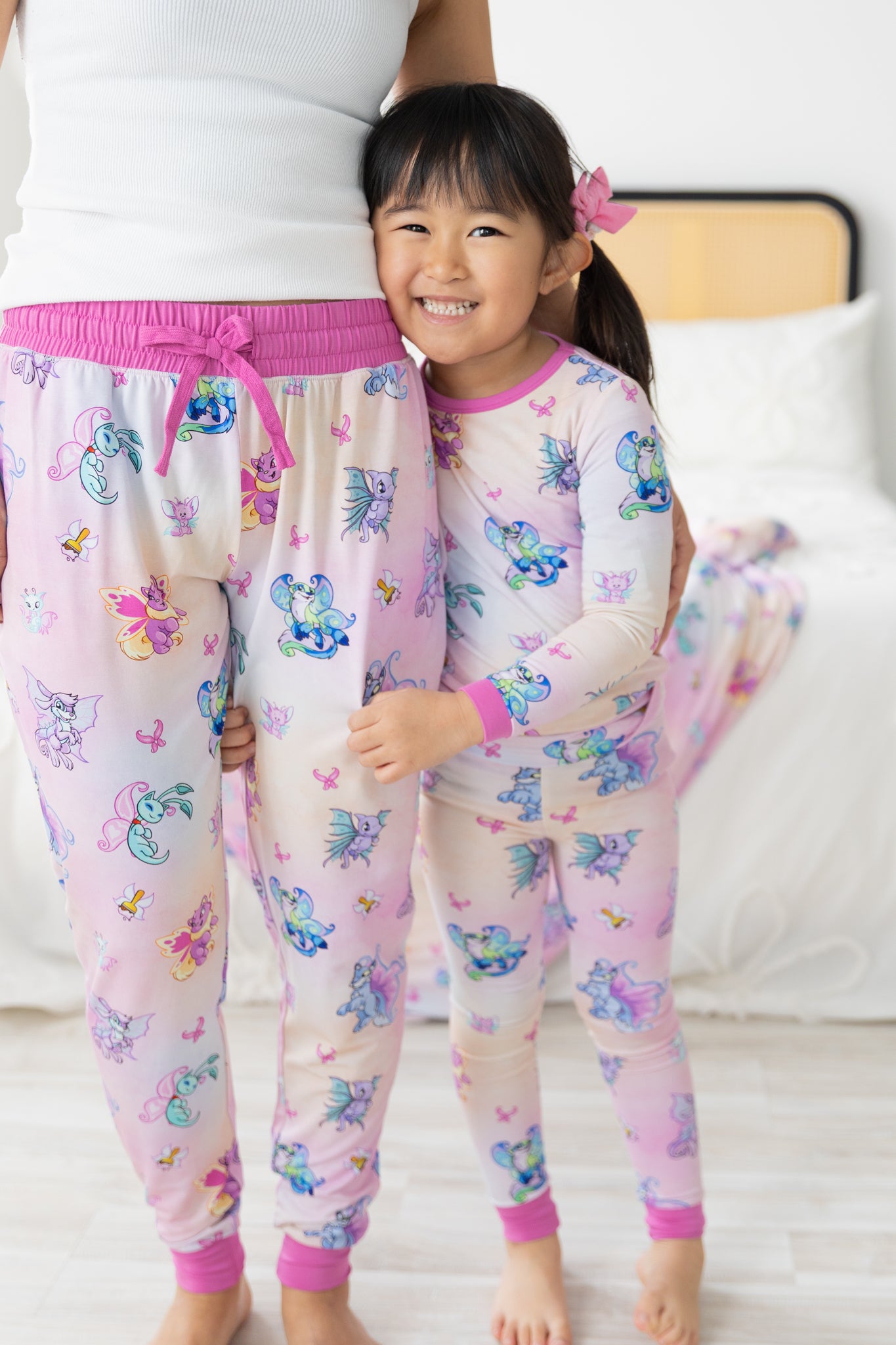 A woman and a child wear matching pink and white jogger pajamas featuring a Neopets Faerie print.