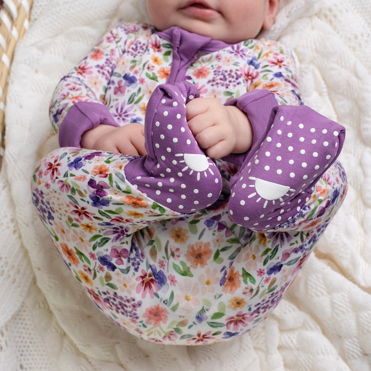 Baby in floral bamboo pajamas with purple polka dot footies.