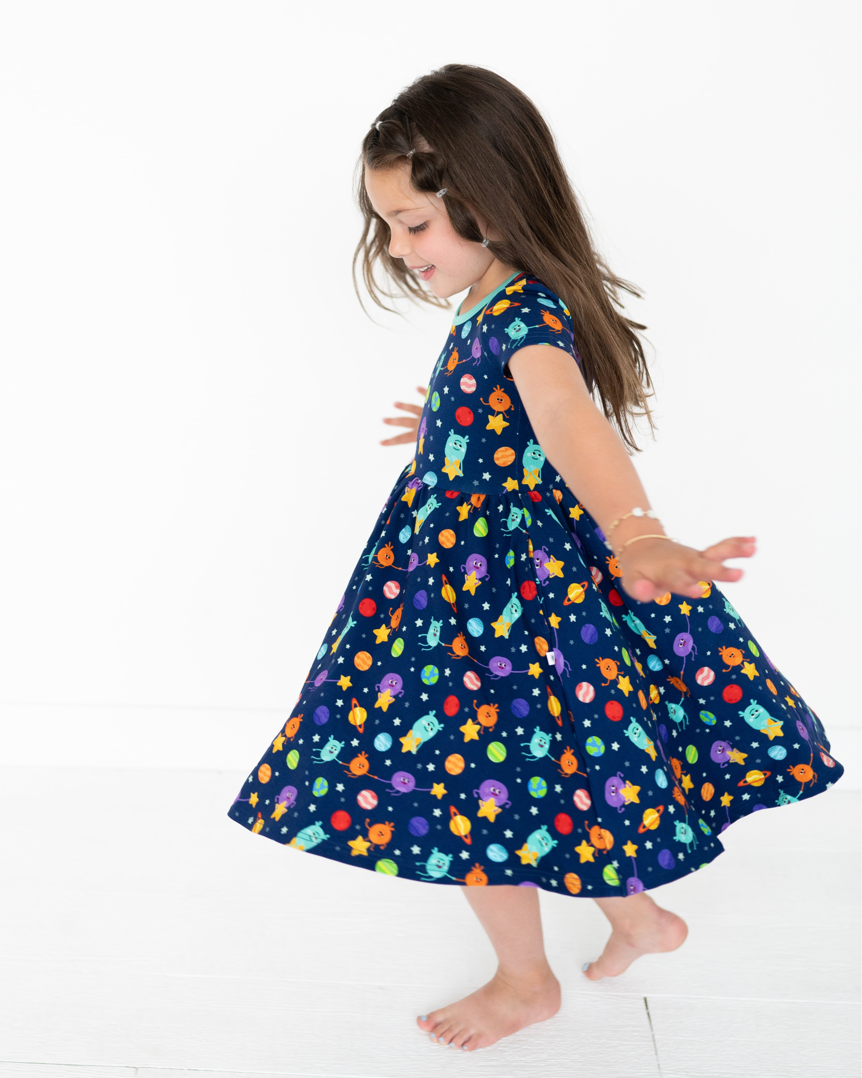 A young girl twirls in a navy blue dress with a space-themed print.