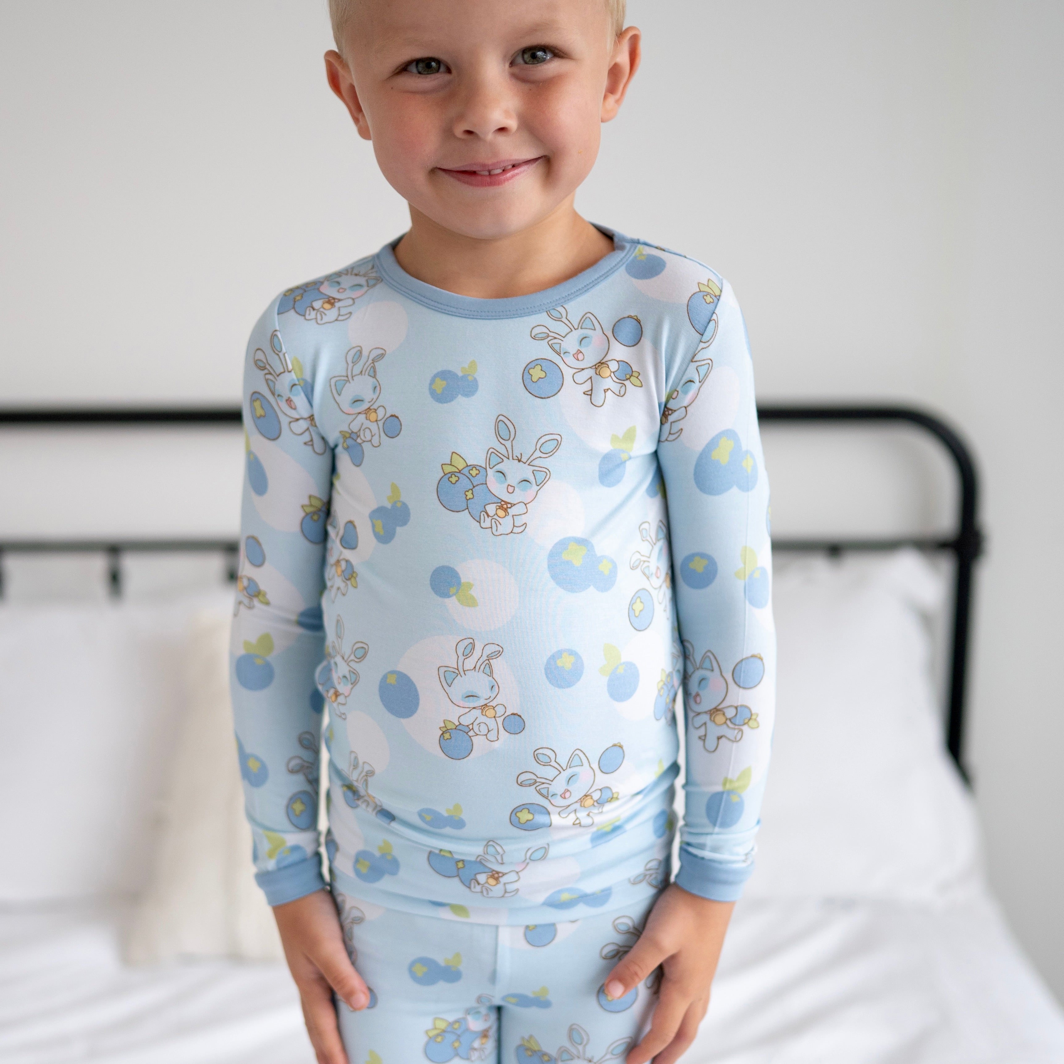 A young boy smiles wearing light blue pajamas with a blueberry and baby Neopets print.