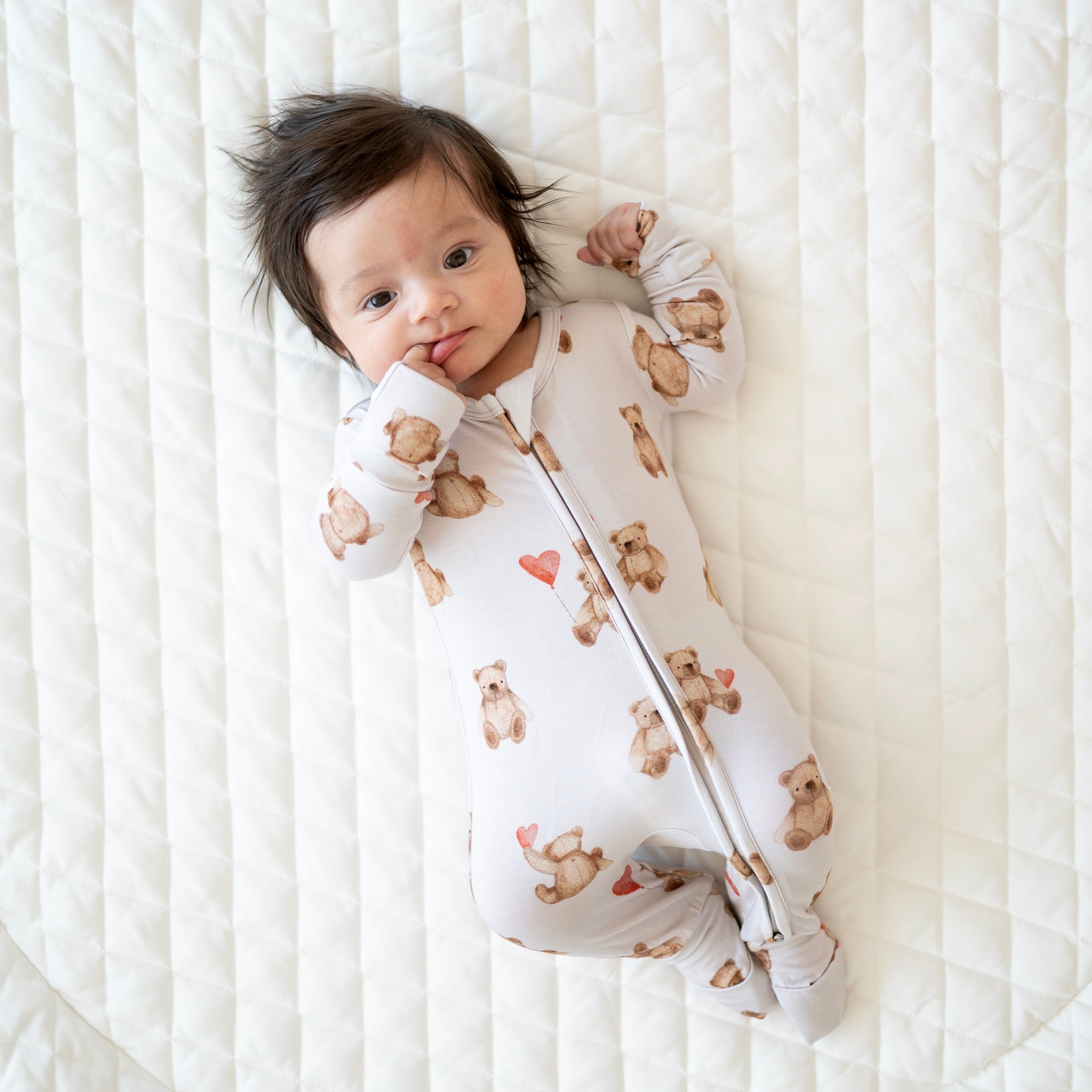 A baby wearing a white footie pajama set with a teddy bear print.